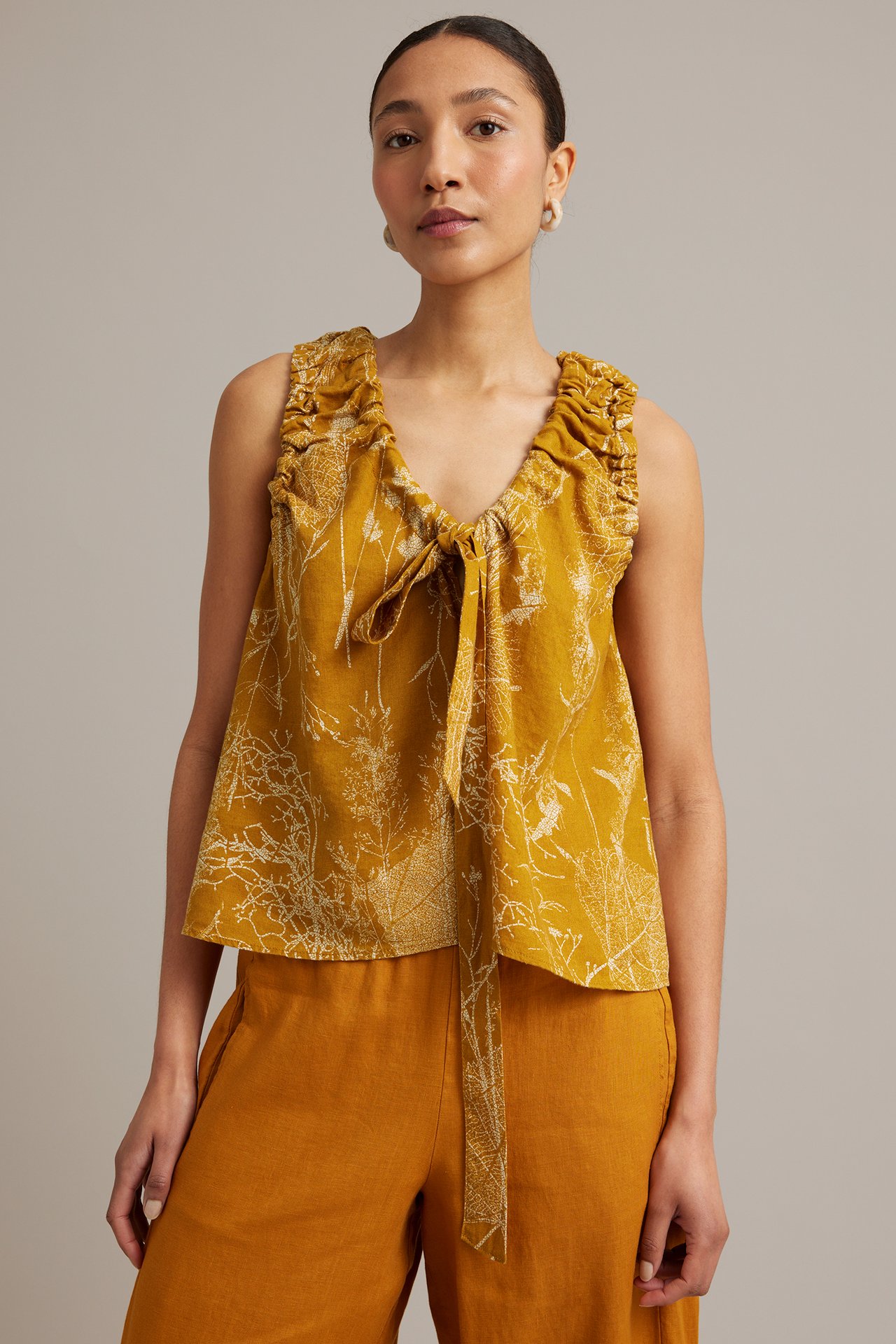 Framifrån, kvinna i gul blommig linnetopp med knytband och matchande linnebyxor.