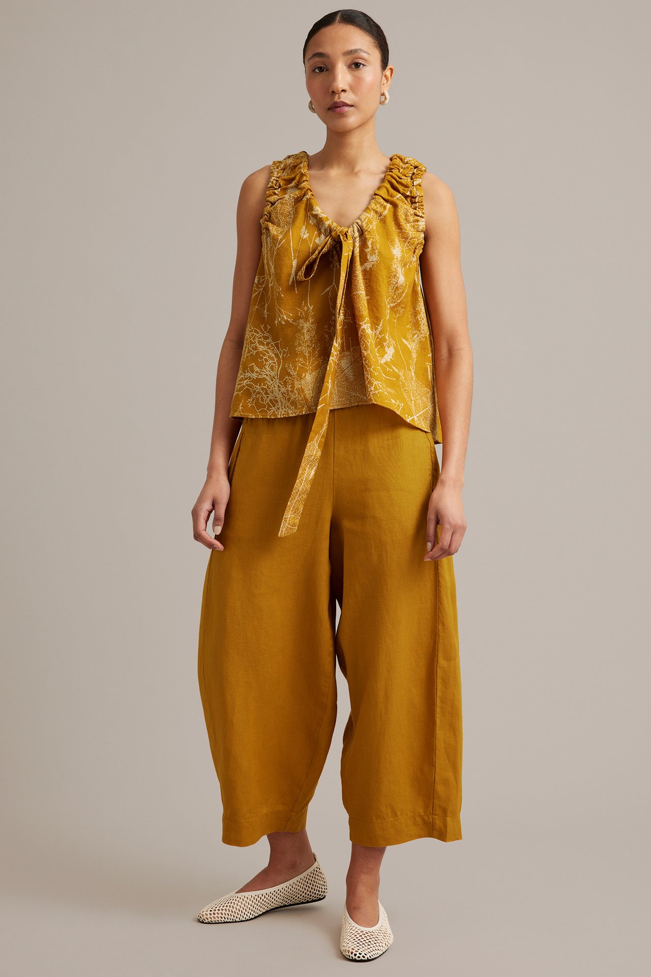 Edestä: nainen keltaisessa kuviollisessa pellavatoppissa solmimisella, samanvärisissä leveissä housuissa ja luonnonvalkoisissa verkkokengissä.