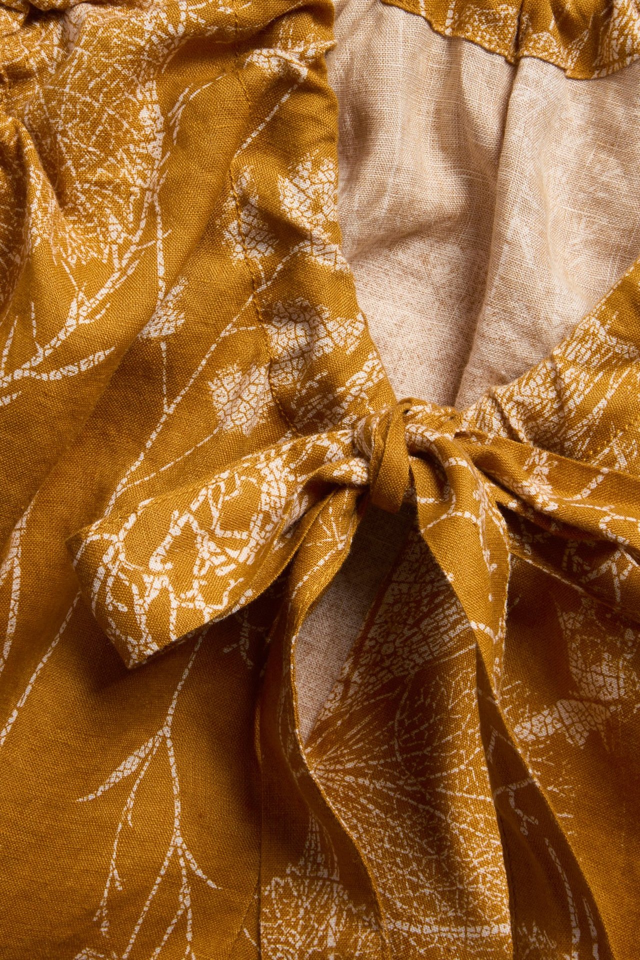 Zbliżenie na żółty lniany top z białym kwiatowym wzorem i wiązanym dekoltem.