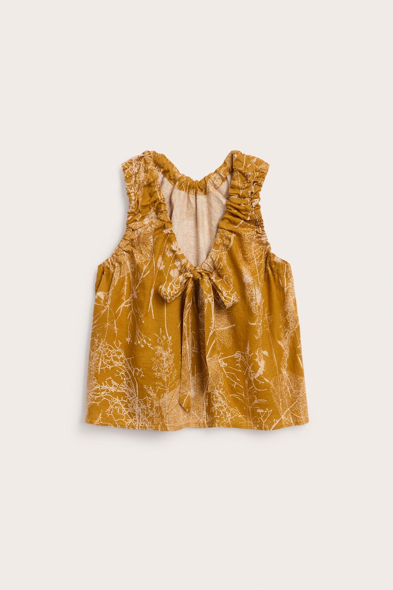 Widok z przodu: Musztardowy lniany top z białym roślinnym wzorem, marszczonym dekoltem i wiązaniem.