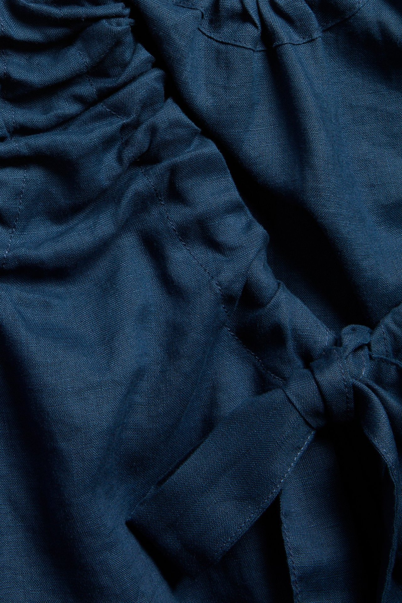 Zbliżenie niebieskiego lnianego topu z dekoltem na troczki i wiązanymi tasiemkami.