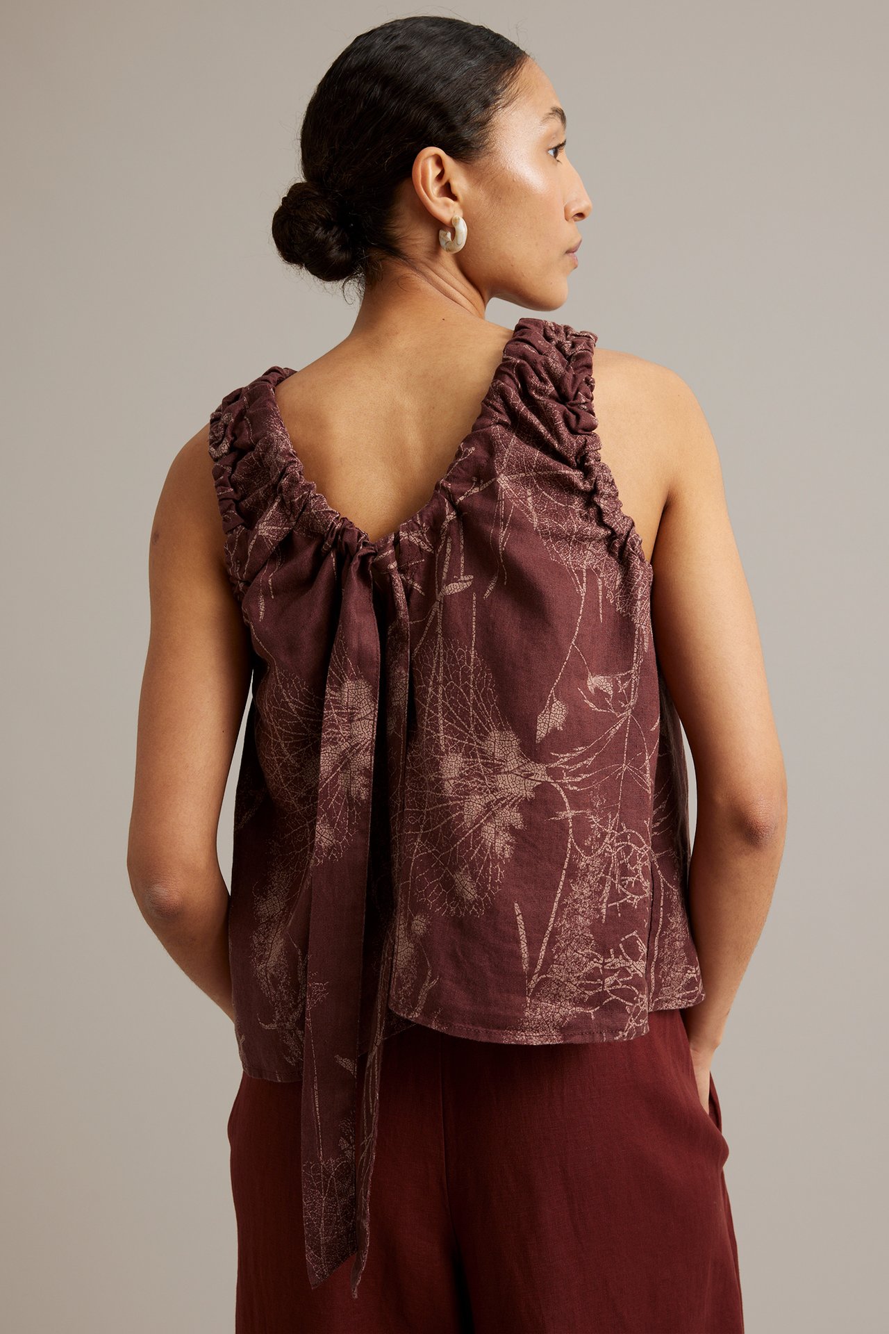 Ryggvy av kvinna i vinröd linnetopp med blommigt mönster och knytband i ryggen, matchas med röda byxor.