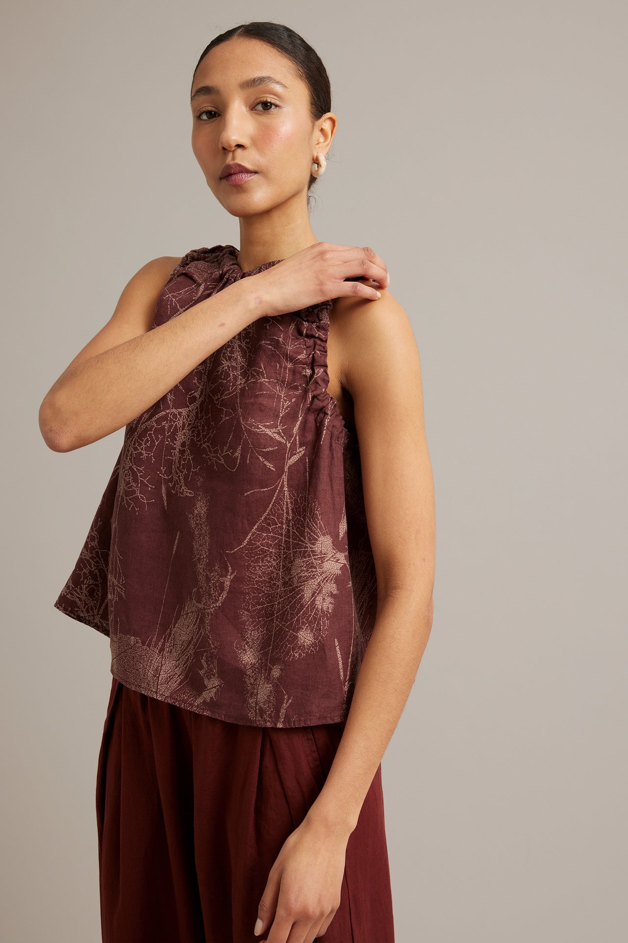 Front view: kvinna i vinröd linnetopp med ljust botaniskt mönster och mörkvinröda vida byxor.