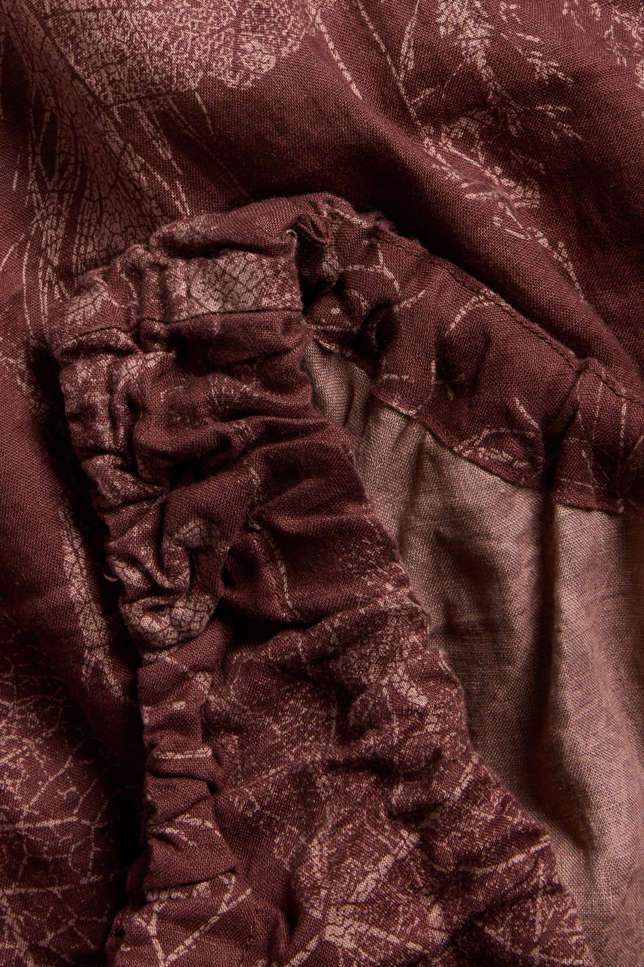 Zbliżenie na bordowy lniany top z jasnym kwiatowym wzorem i marszczonymi detalami.