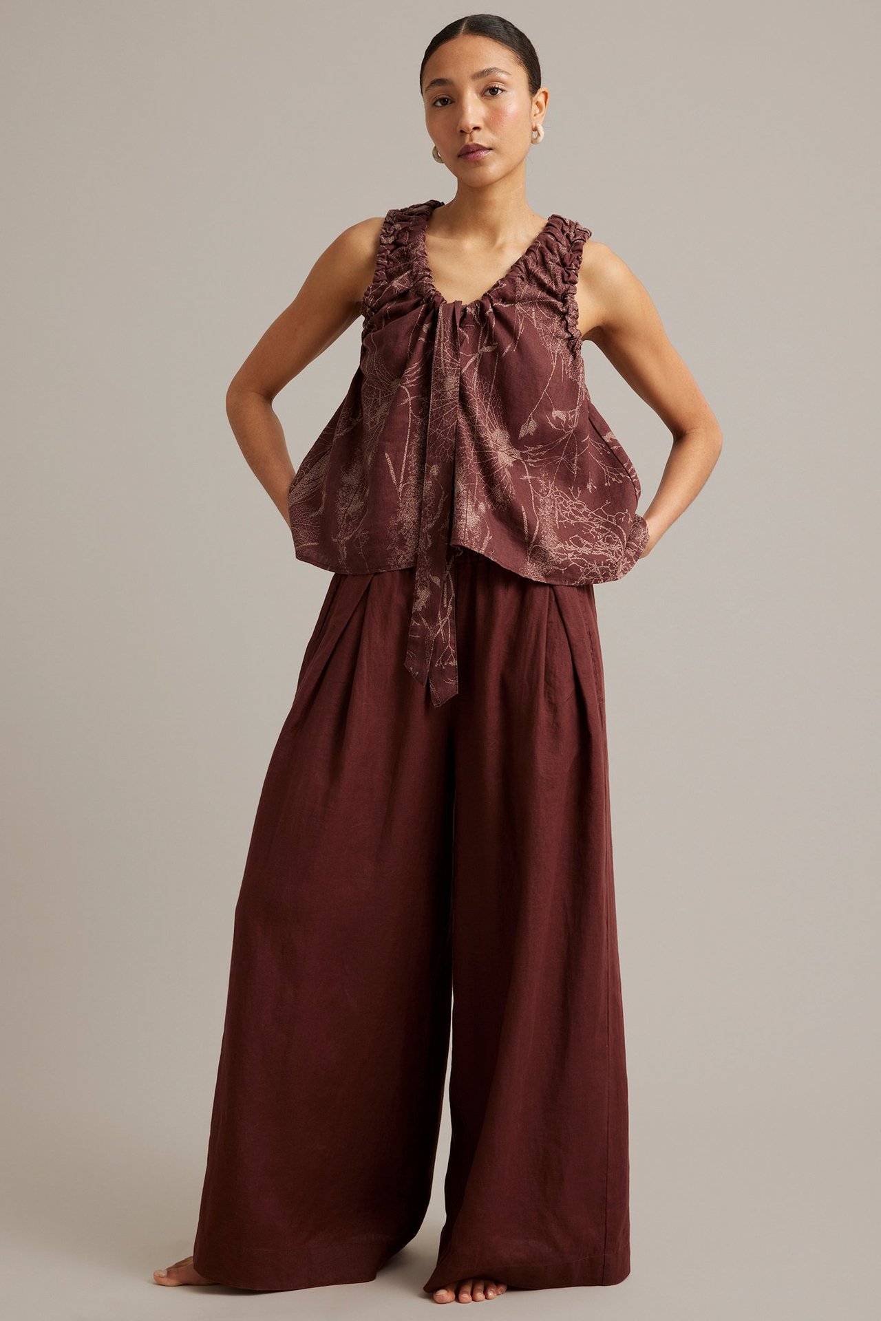 Framifrån: kvinna i vinröd blommig linnetopp, knytband och vida linnebyxor.