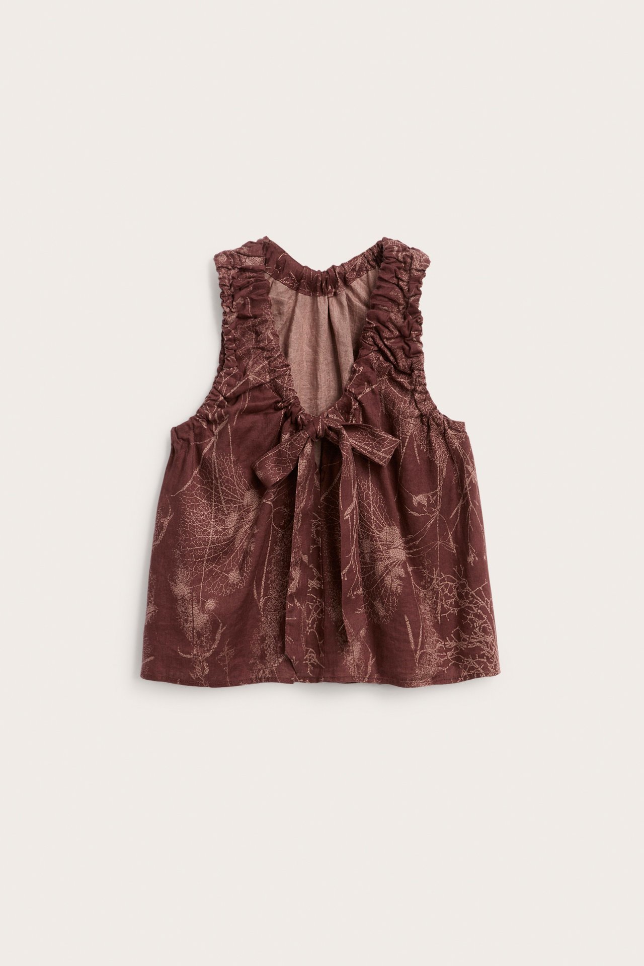 Widok z przodu: luźny damski top z czerwonego lnu z jasnym wzorem liści, marszczonym dekoltem w serek i wiązaniem.