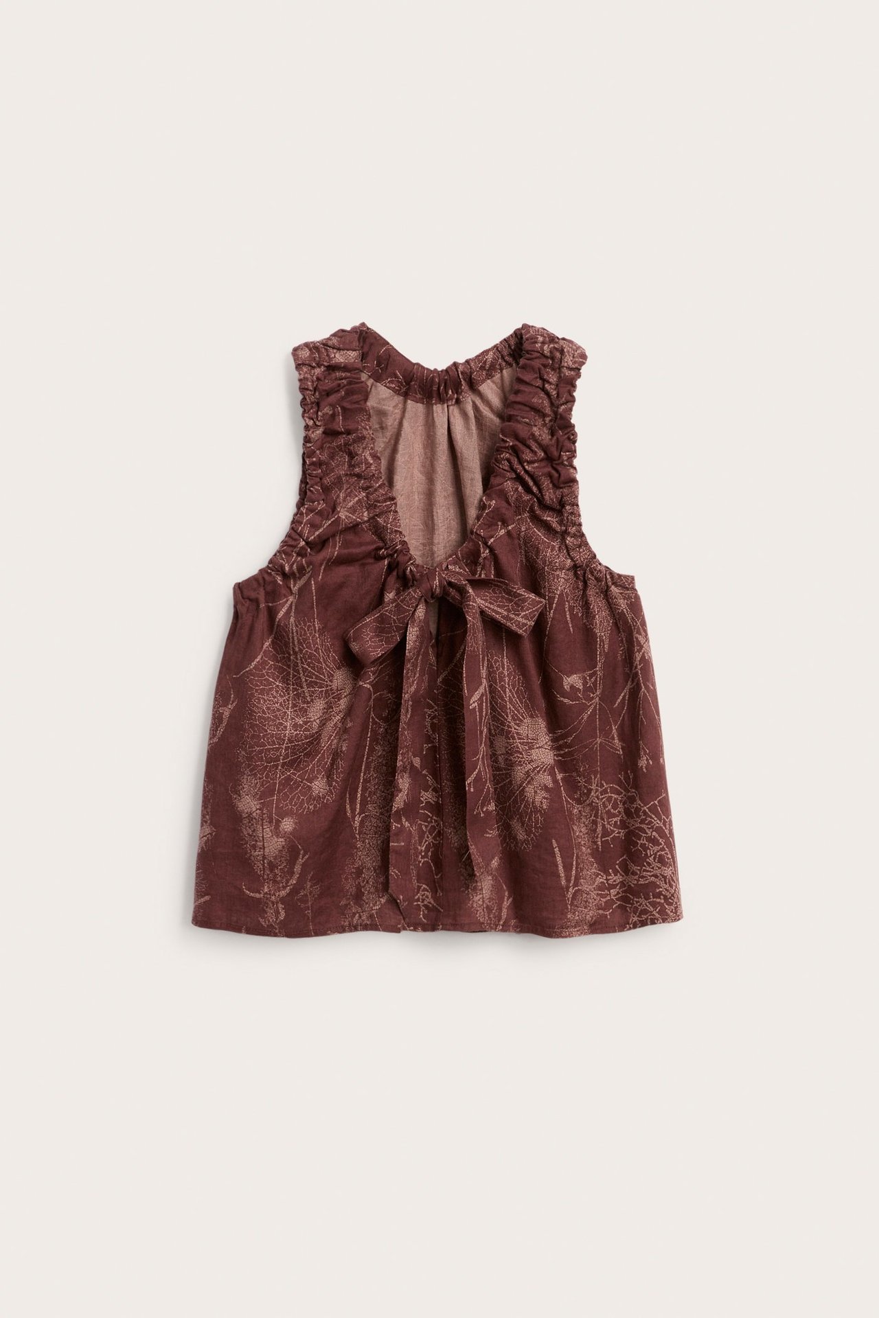 Widok z przodu: luźny damski top z czerwonego lnu z jasnym wzorem liści, marszczonym dekoltem w serek i wiązaniem.