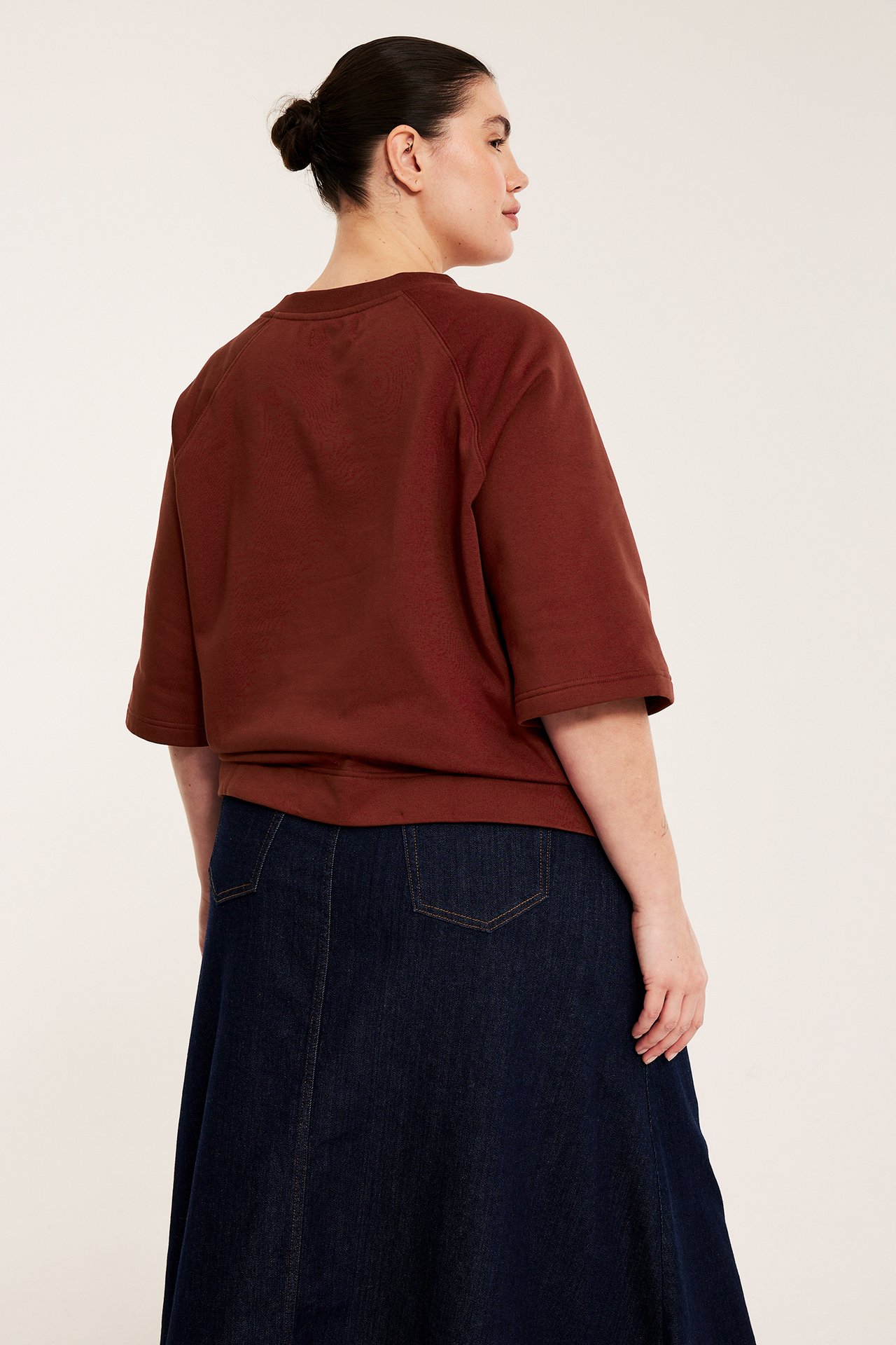 Naisen taka-sivukuva, yllään punainen lyhythihainen collegepaita tummansinisen farkkuhameen kanssa.