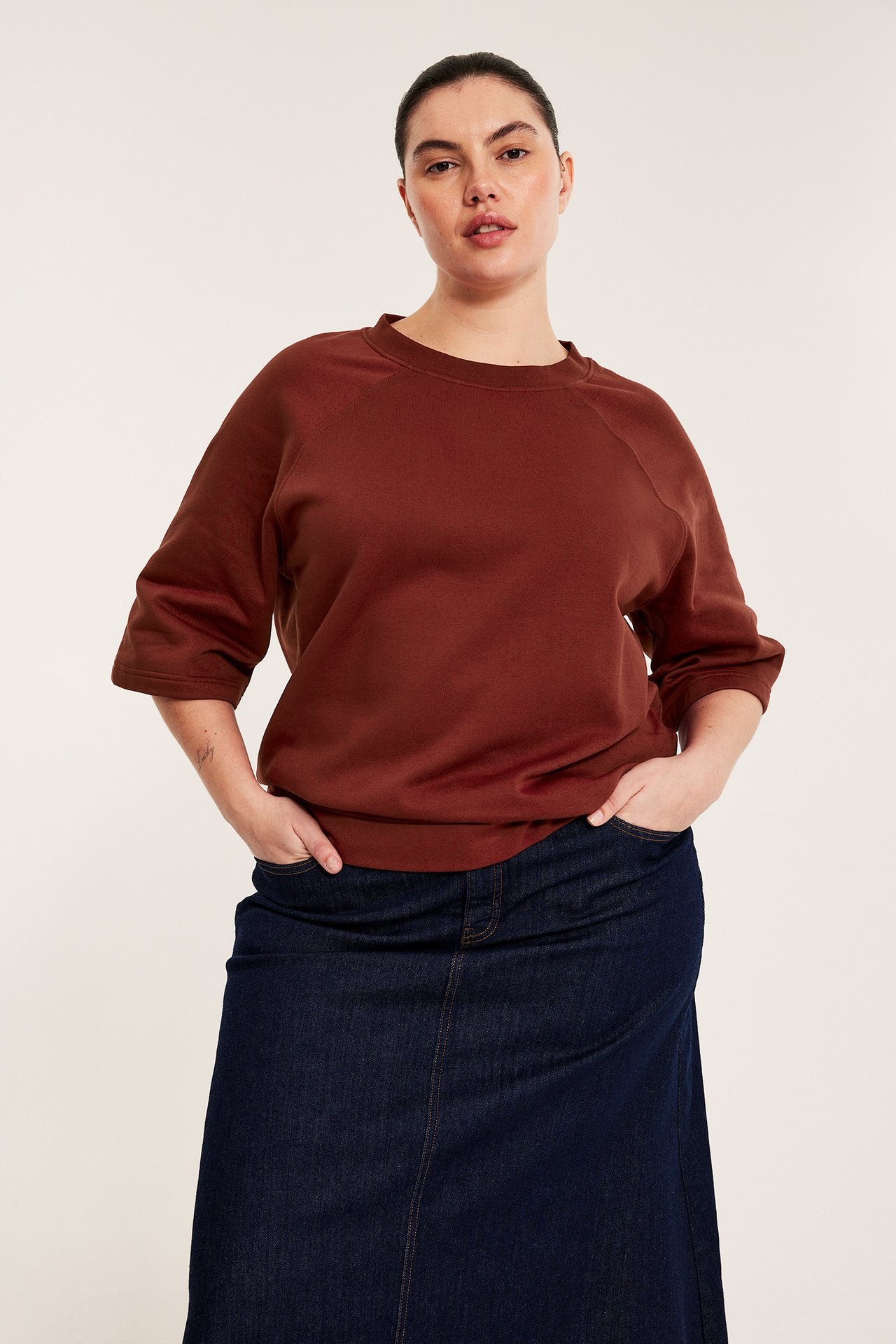 Edestäpäin: nainen ruosteenpunaisessa lyhythihaisessa collegepaidassa ja tummansinisessä farkkuhameessa.