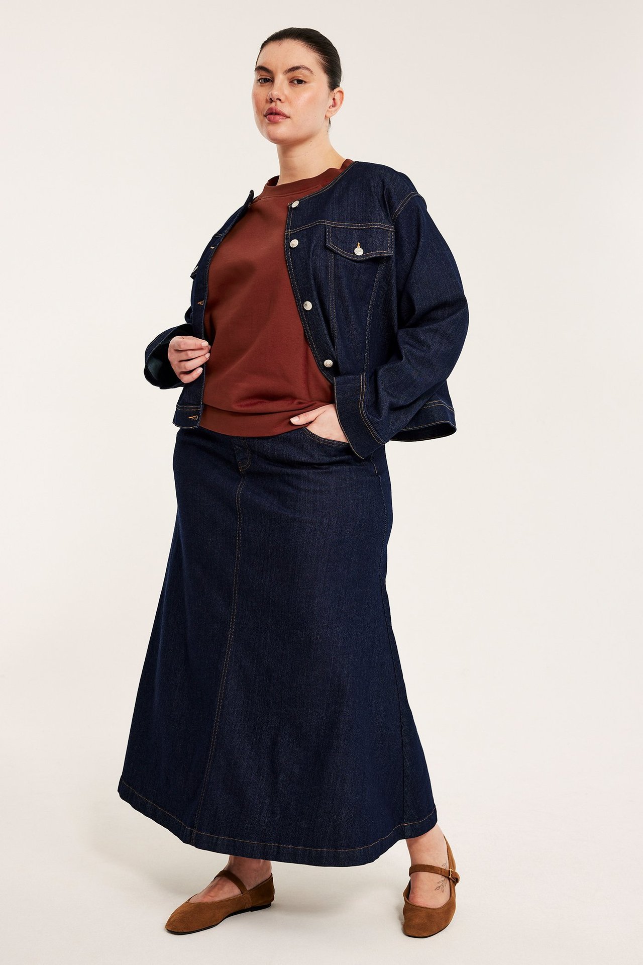 Edestä: nainen punaruskeassa lyhythihaisessa collegepaidassa, tummansinisessä farkkutakissa, farkkumaksihameessa ja ruskeissa ballerinoissa.