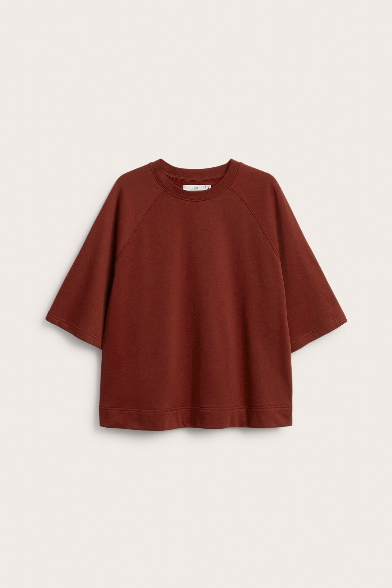 Edestäpäin löysä, yksivärinen punainen lyhythihainen collegepaita, jossa pyöreä pääntie ja leveät hihat.