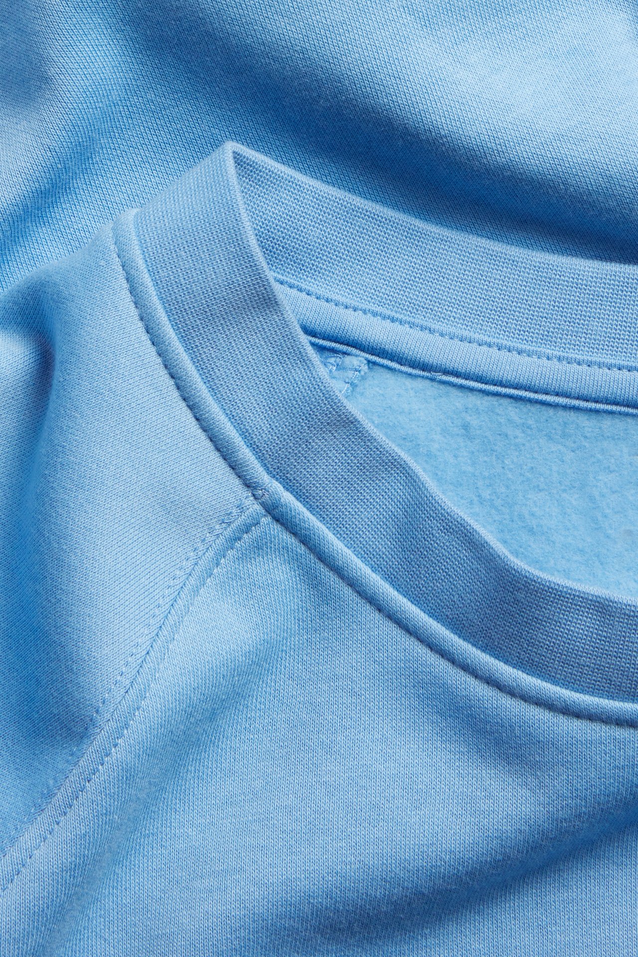 Lähikuva vaaleansinisestä lyhythihaisesta collegepaidasta, jossa näkyy resori pääntie ja harjattu sisäpuoli.