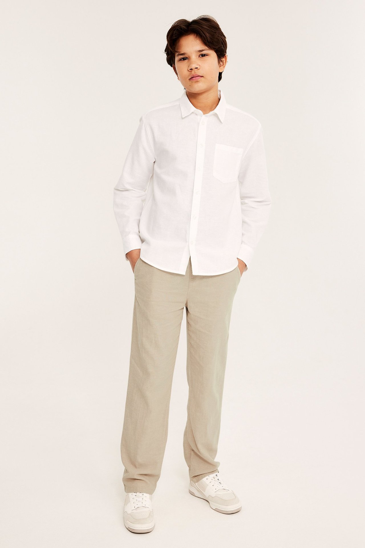 Przód: dziecko w beżowych, luźnych spodniach z lnu, białej koszuli z długim rękawem i białych tenisówkach.