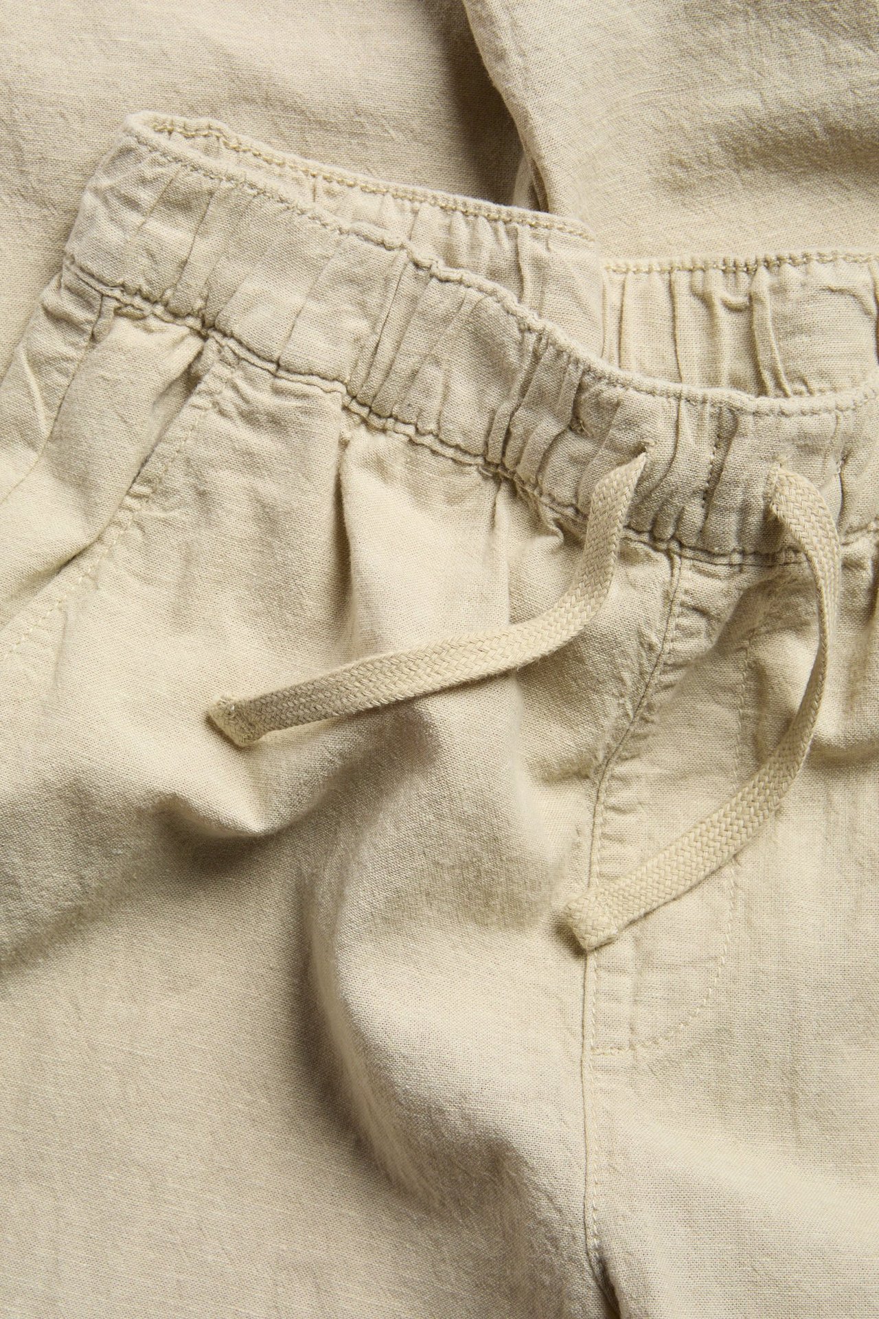 Zbliżenie beżowych spodni dziecięcych z domieszką lnu, z elastycznym pasem i sznurkiem.