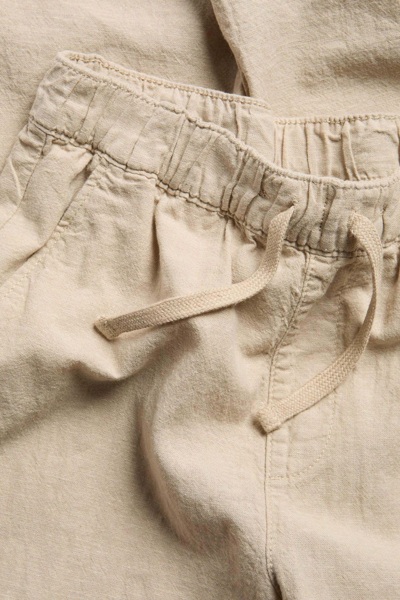 Zbliżenie beżowych spodni z mieszanki lnu z elastyczną talią ze sznurkiem i bocznymi kieszeniami.