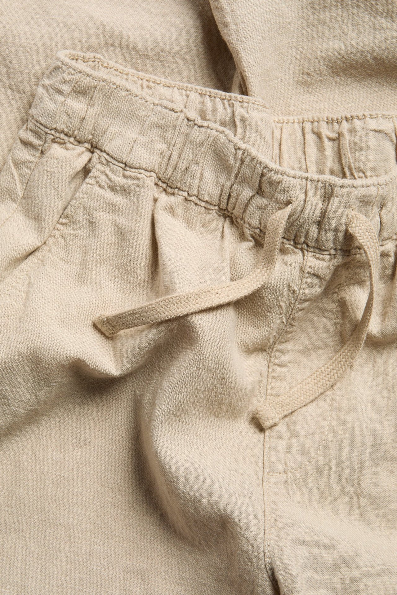 Zbliżenie beżowych spodni z mieszanki lnu z elastyczną talią ze sznurkiem i bocznymi kieszeniami.