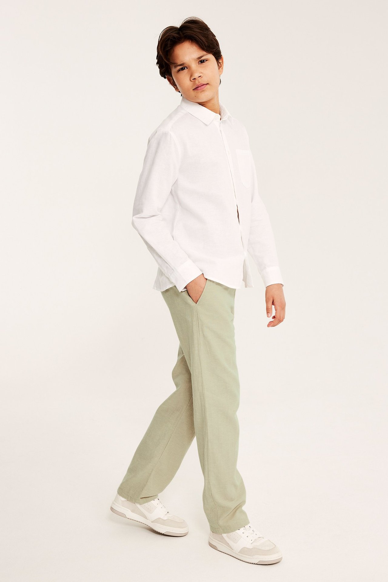 Edestäpäin: lapsi yllään rennot beiget pellavasekoitehousut, valkoinen pitkähihainen paita ja valkoiset tennarit.