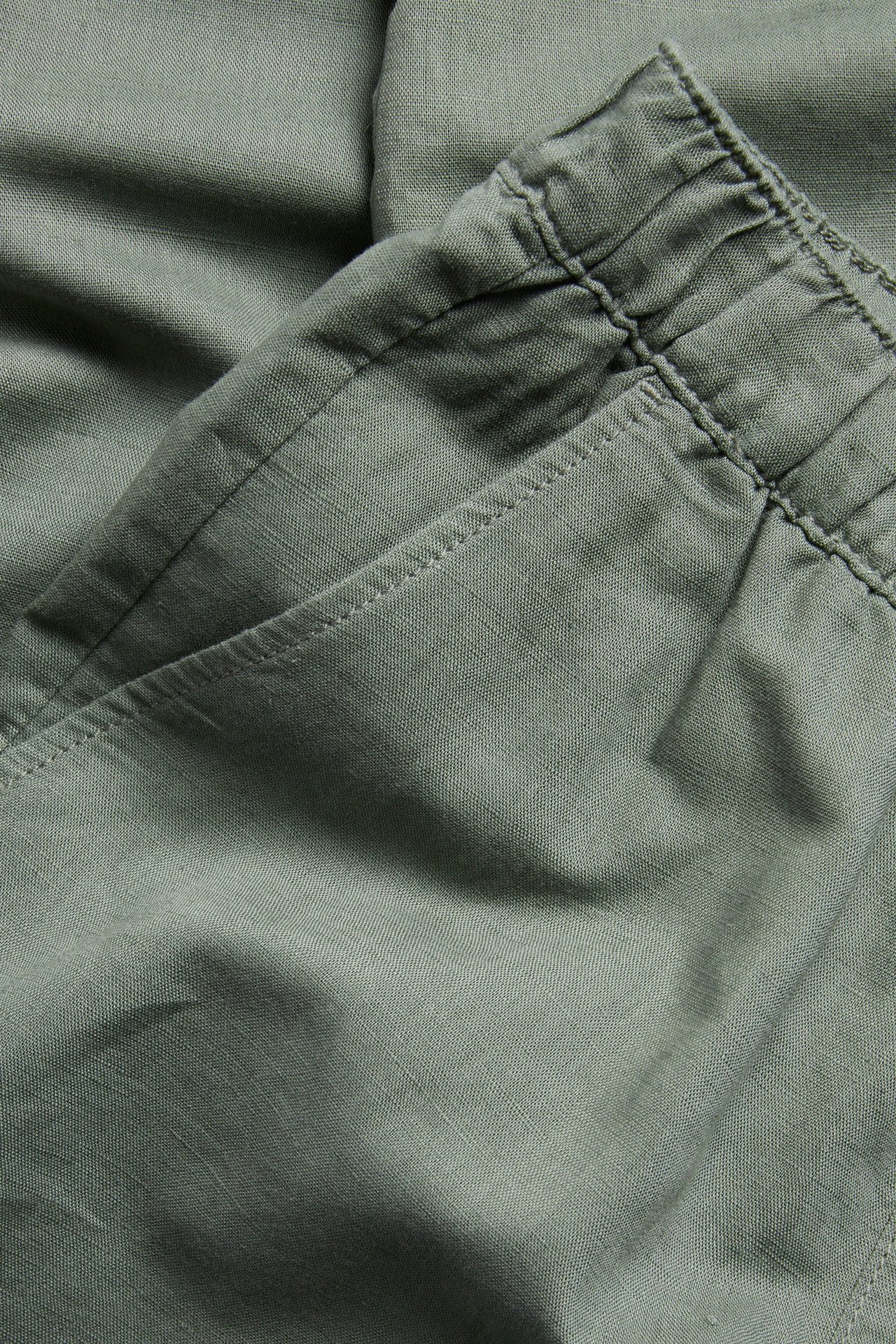 Zbliżenie oliwkowo-zielonych spodni z mieszanki lnu, z elastyczną talią i boczną kieszenią.