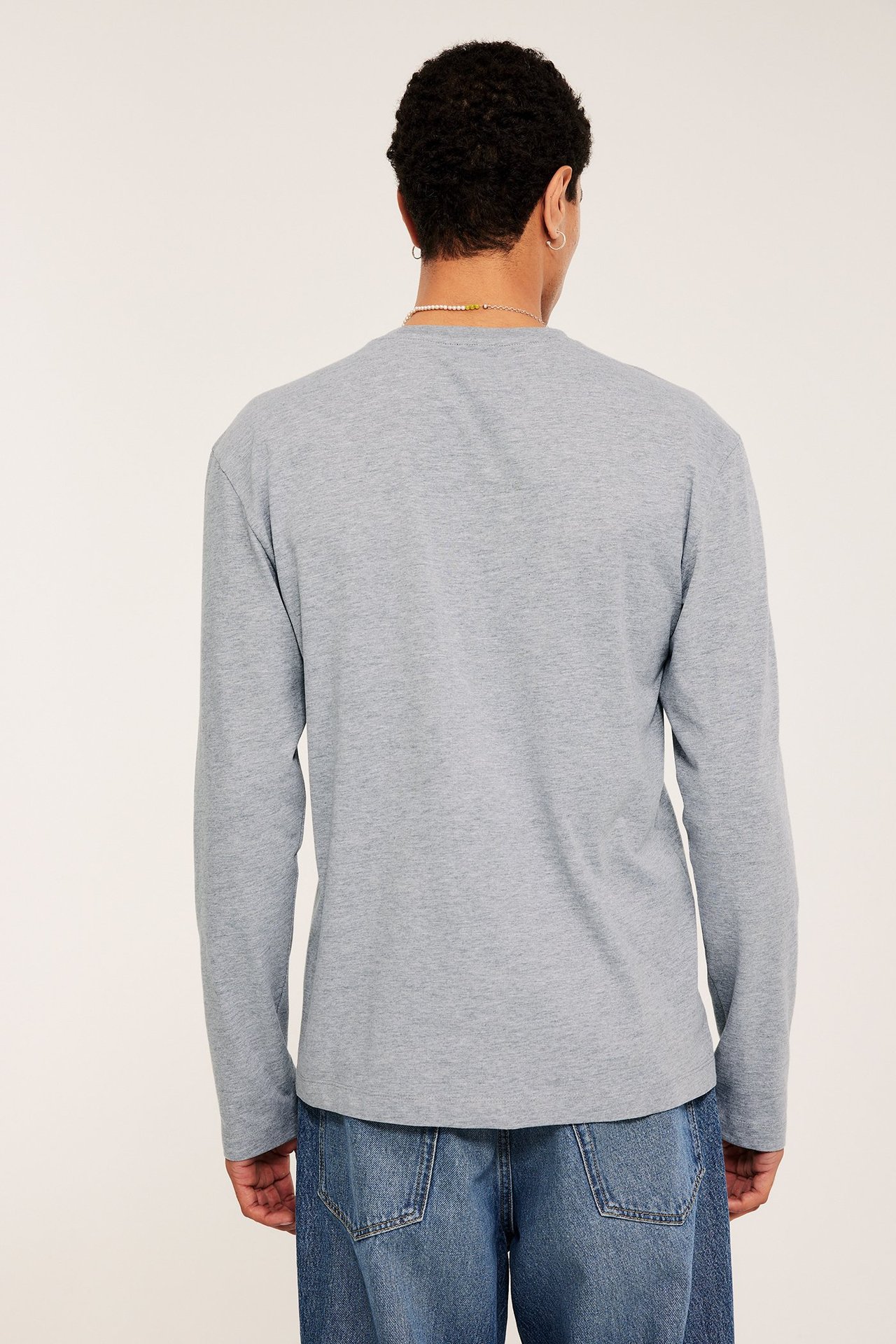Mężczyzna od tyłu w jasnoszarym t-shircie z długim rękawem i niebieskich jeansach.