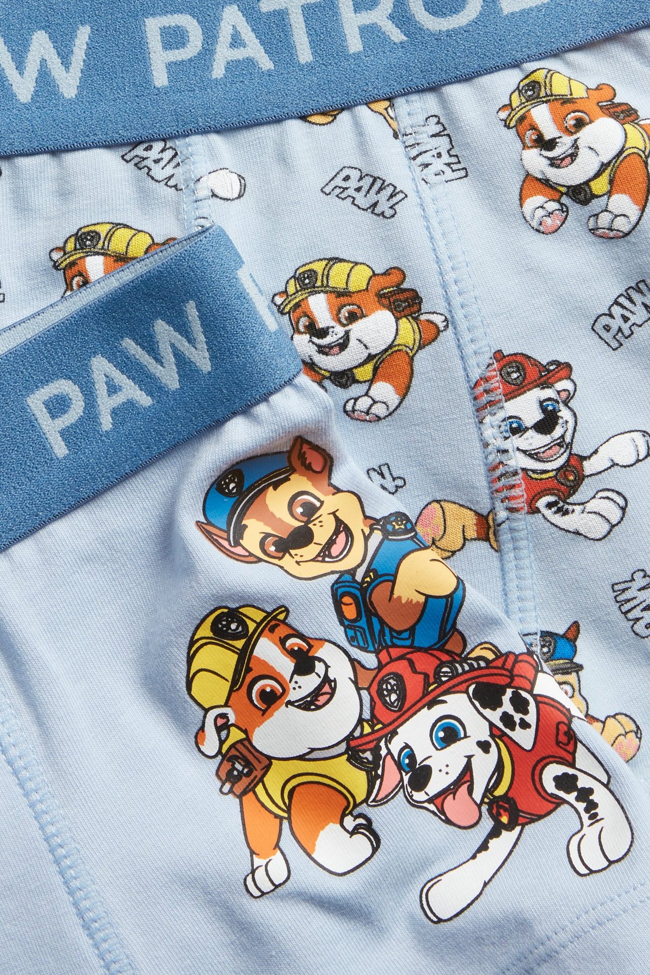 Zbliżenie, ukośny widok na jasnoniebieskie bokserki dziecięce we wzór Psi Patrol z elastycznym pasem.