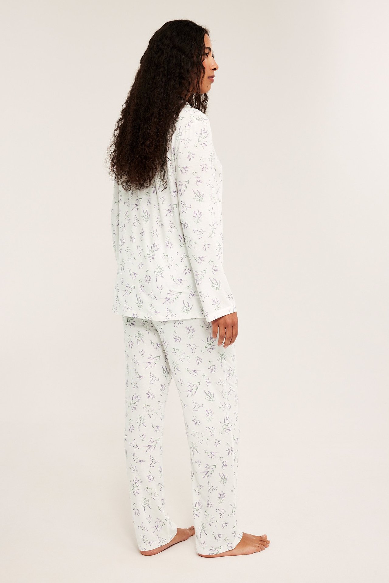 Sideutsikt av en kvinne i en lys, ledig pyjamas med lilla blomstermønster.