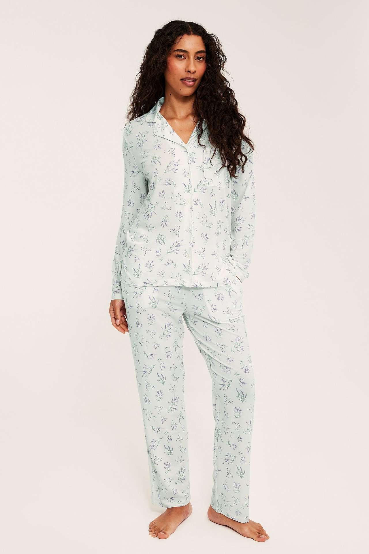 Edestä: Nainen vaaleanliilassa kuviollisessa lyocell-pyjamassasetissä, jossa kauluspaita ja suorat housut.