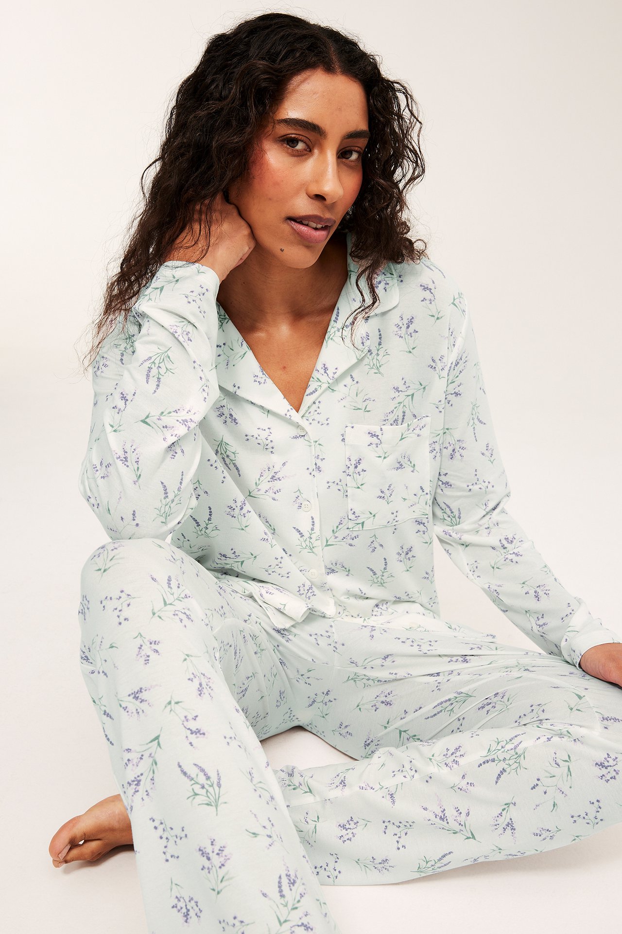 Edestäpäin nainen yllään vaaleanlila lyocellpyjamas laventelin kukkakuviolla ja tereyksityiskohdilla.