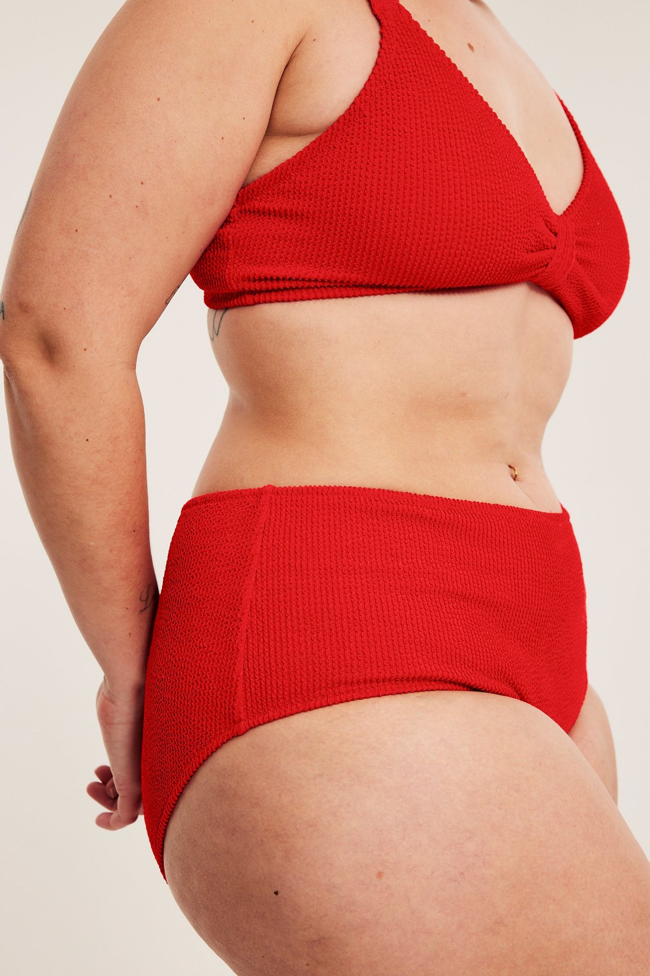 Widok z boku: kobieta w czerwonych, teksturowanych majtkach bikini hipster i pasującym topie.
