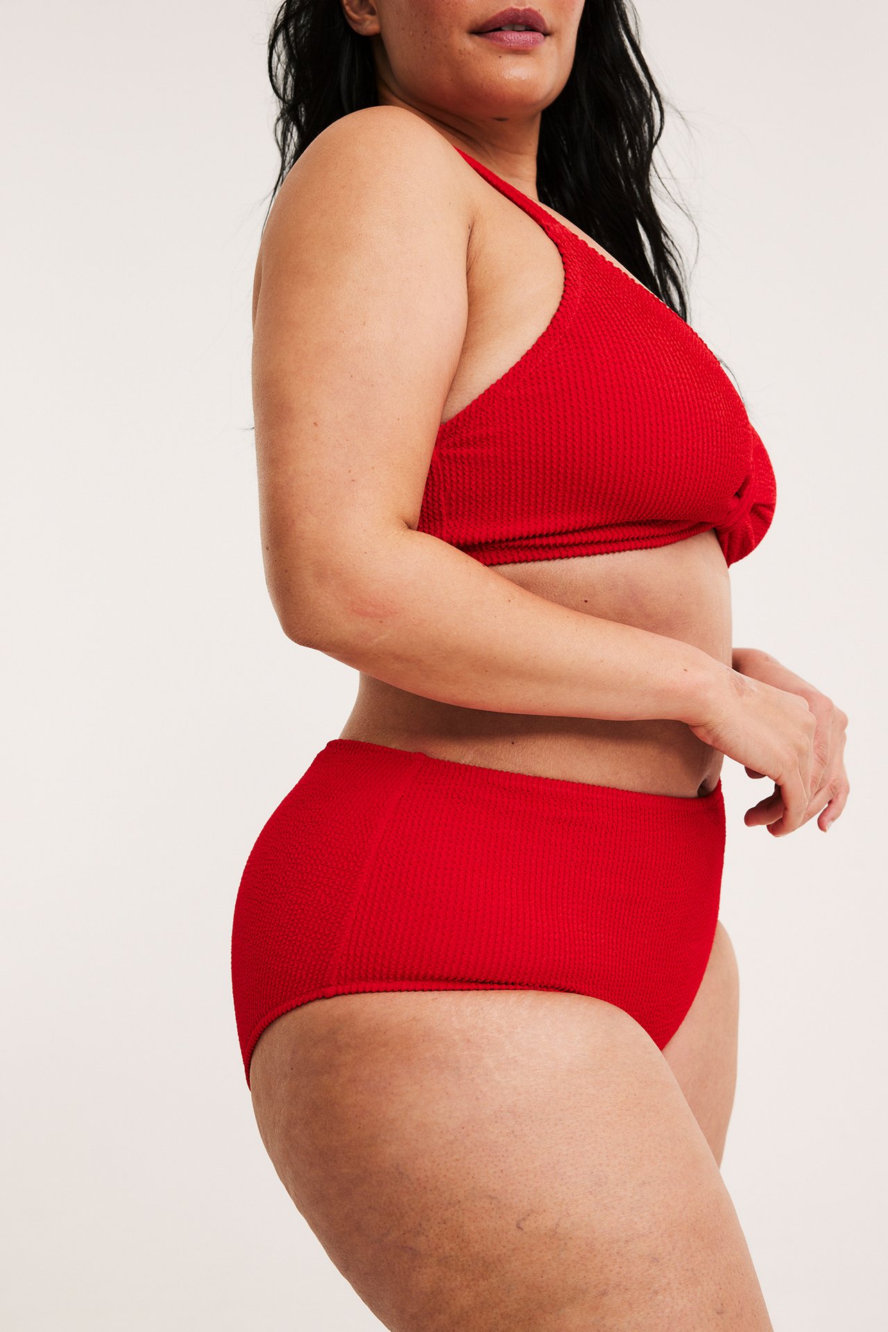 Sidovy av kvinna i röd, strukturerad, högmidjad bikinitrosa och matchande bikiniöverdel.