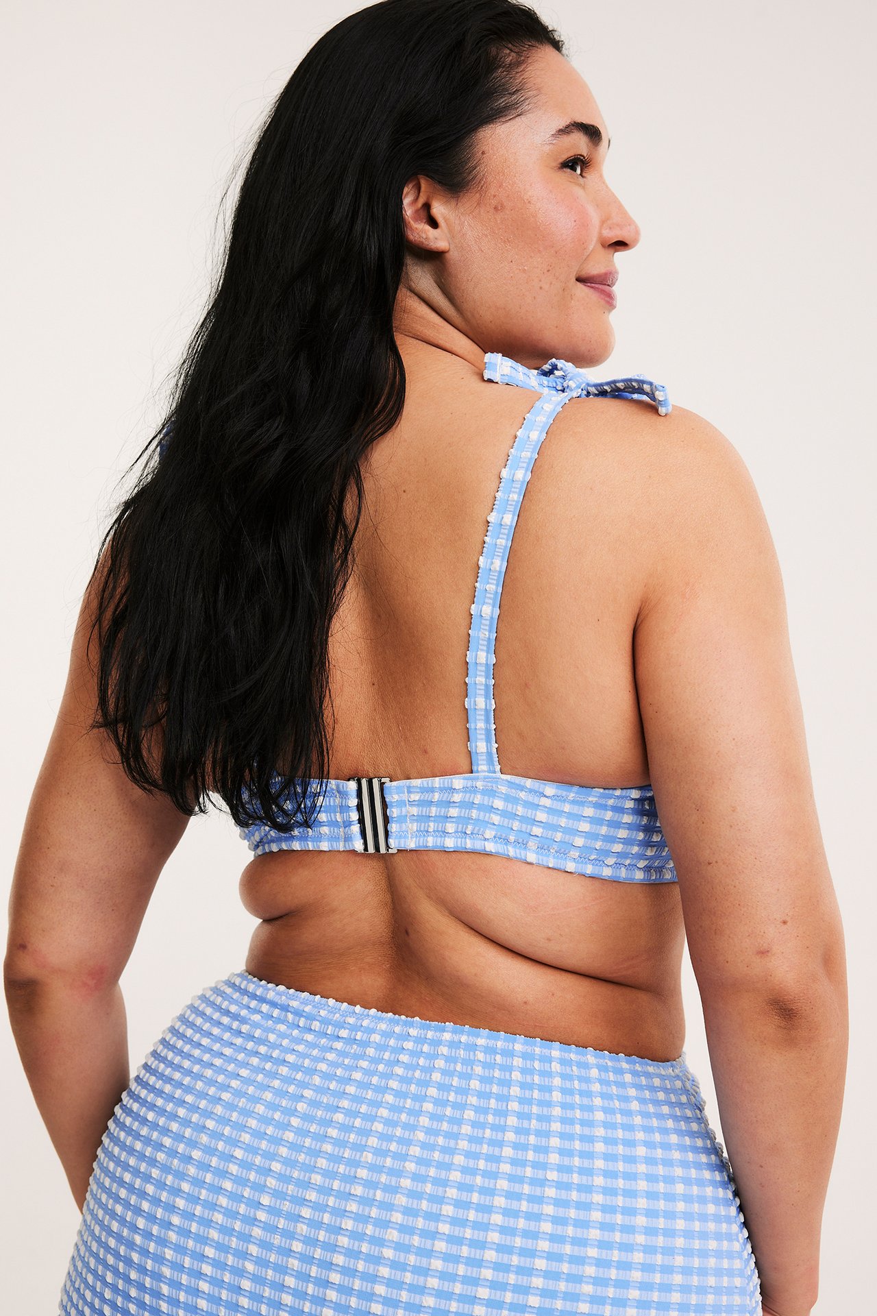 Bakifrån på kvinna i blåvitrutig balconette-bh med knytband och matchande trosa.