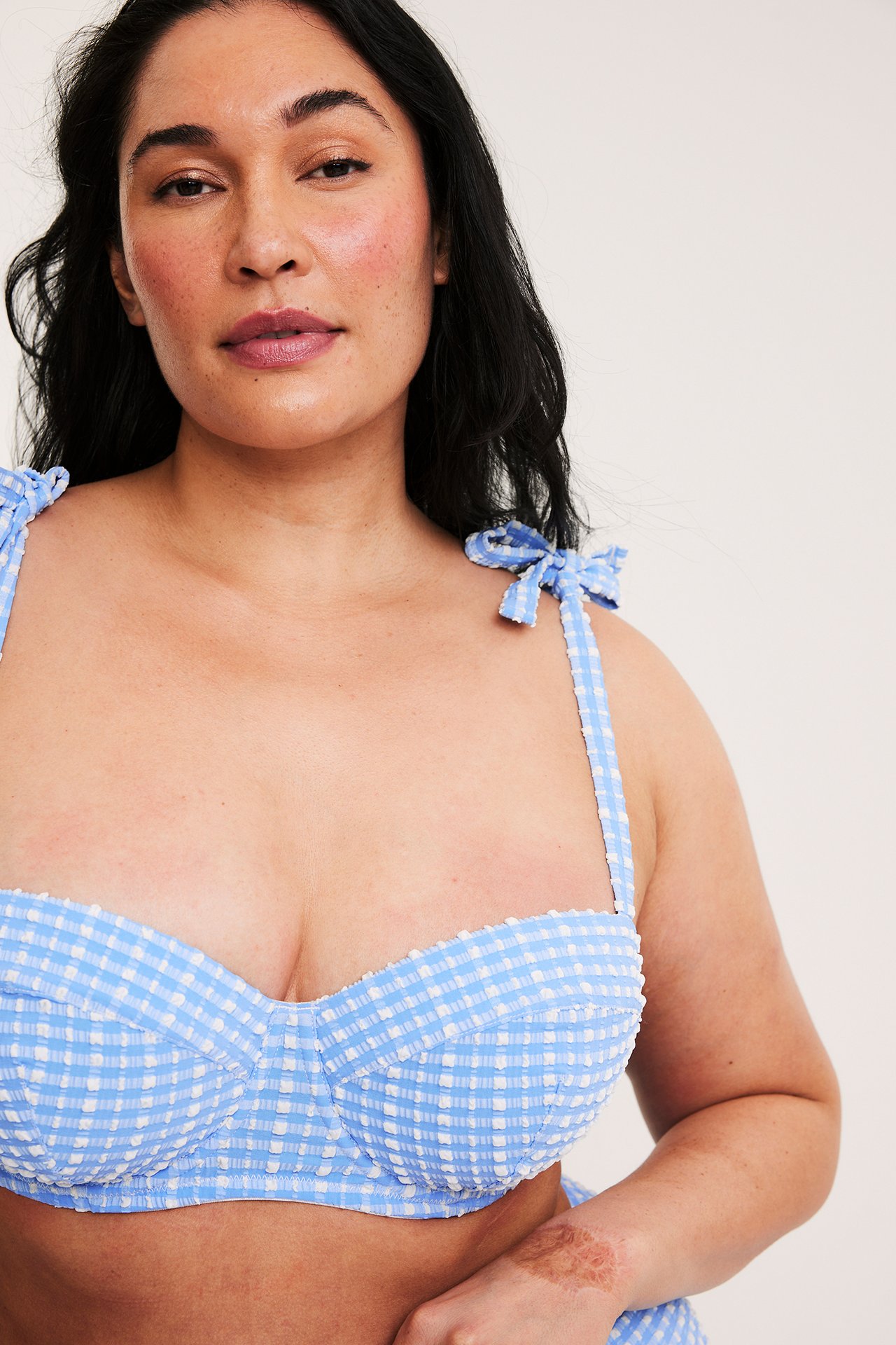 Frontutsikt av en kvinne iført en blå og hvit rutete balconette bikini-topp med knytebånd.