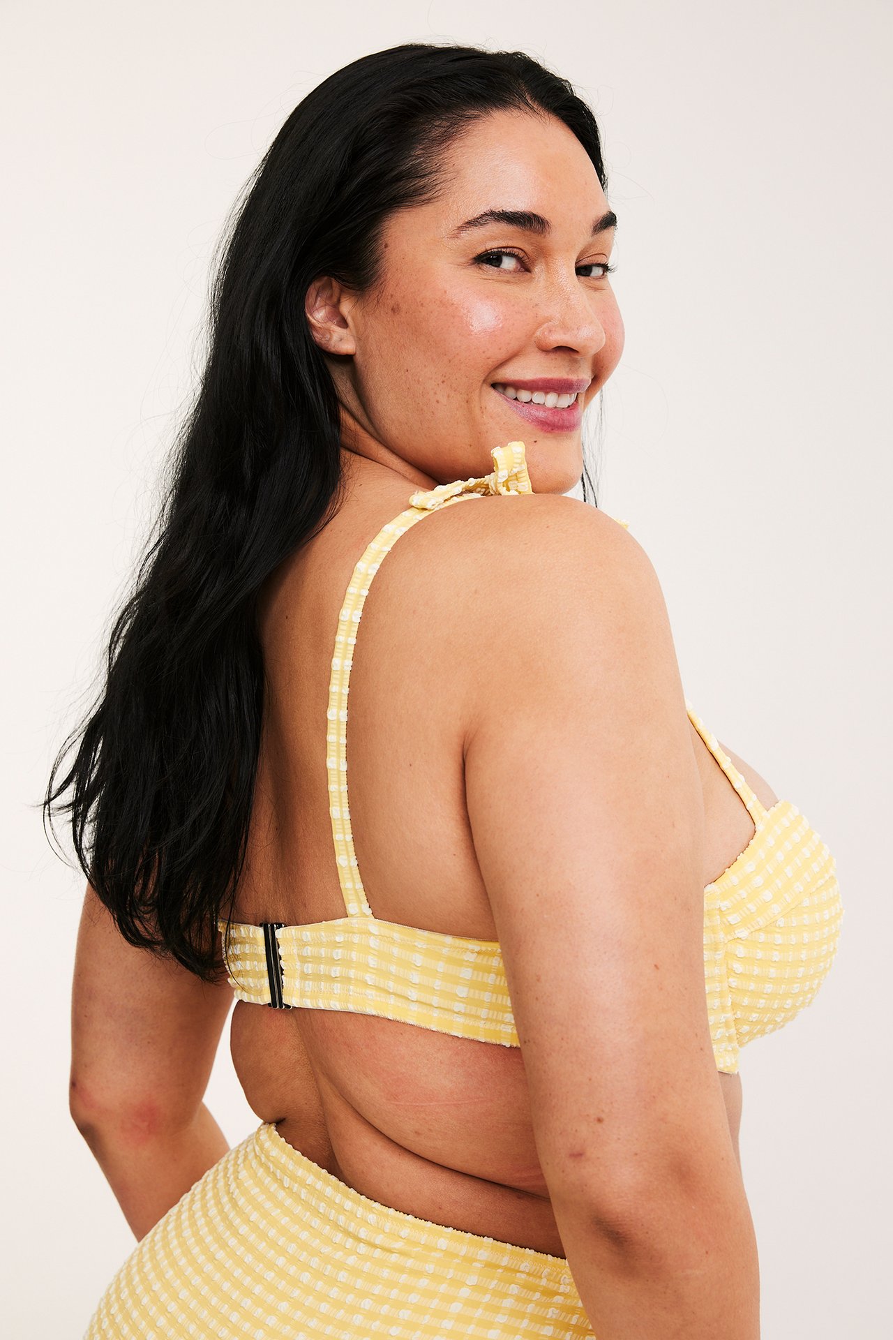 Sidebilde av smilende kvinne i gulrutet balconette bikinitopp med knytestropper og matchende underdel.