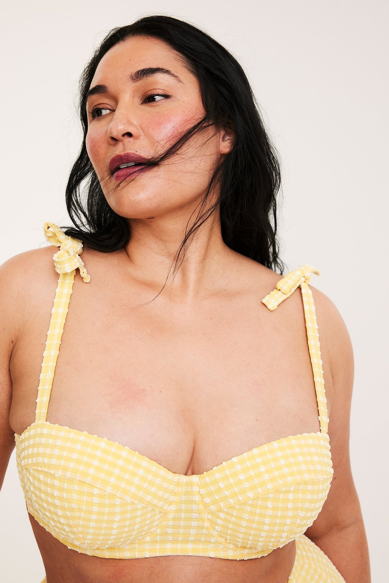 Naisen edestä näkymä, keltainen ruudullinen balconette-bikiniyläosa solmittavilla olkaimilla.