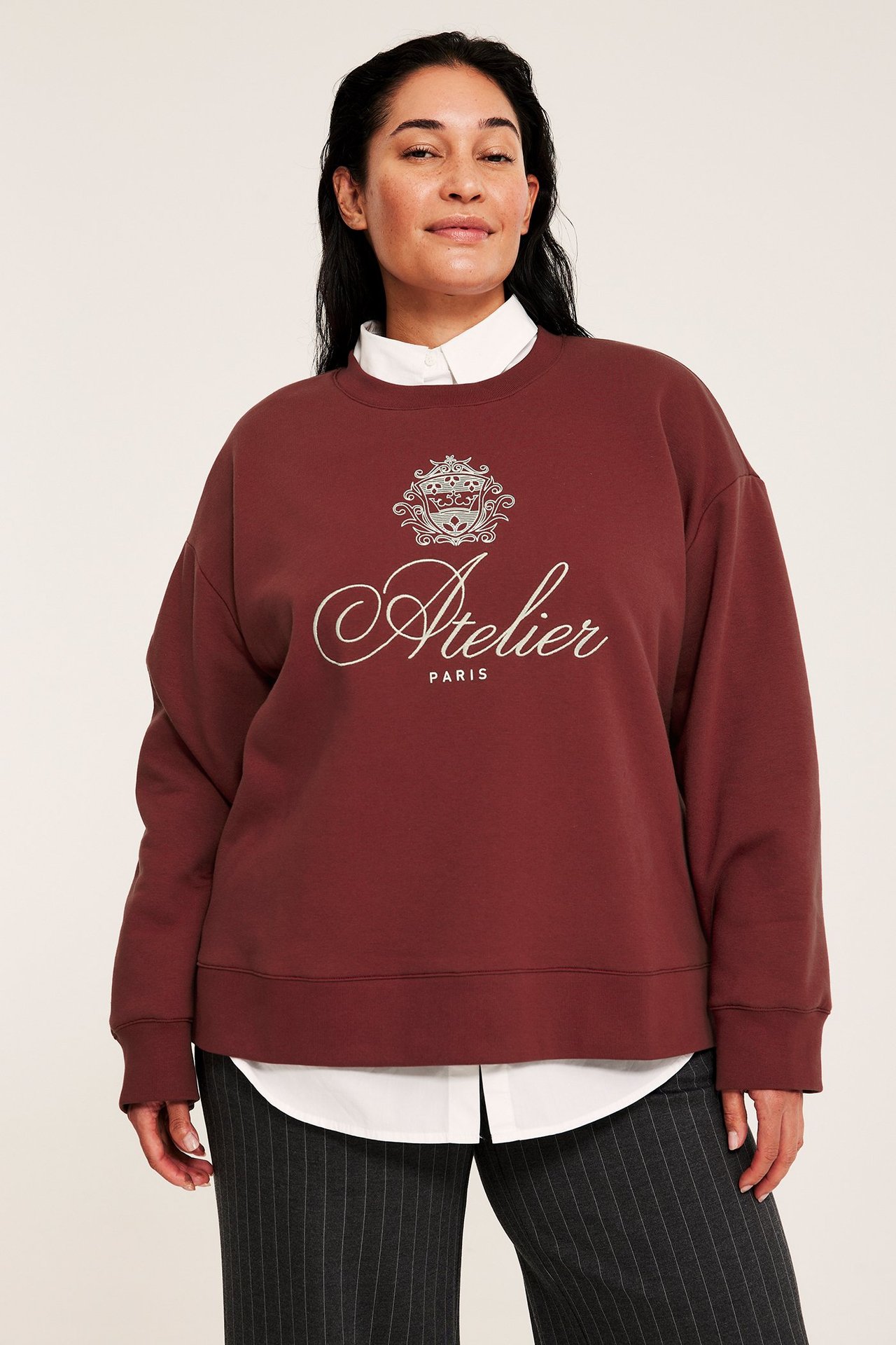 Widok z przodu: Kobieta w czerwonej bluzie z białym wzorem 'Atelier Paris', na białej koszuli i spodniach w paski.