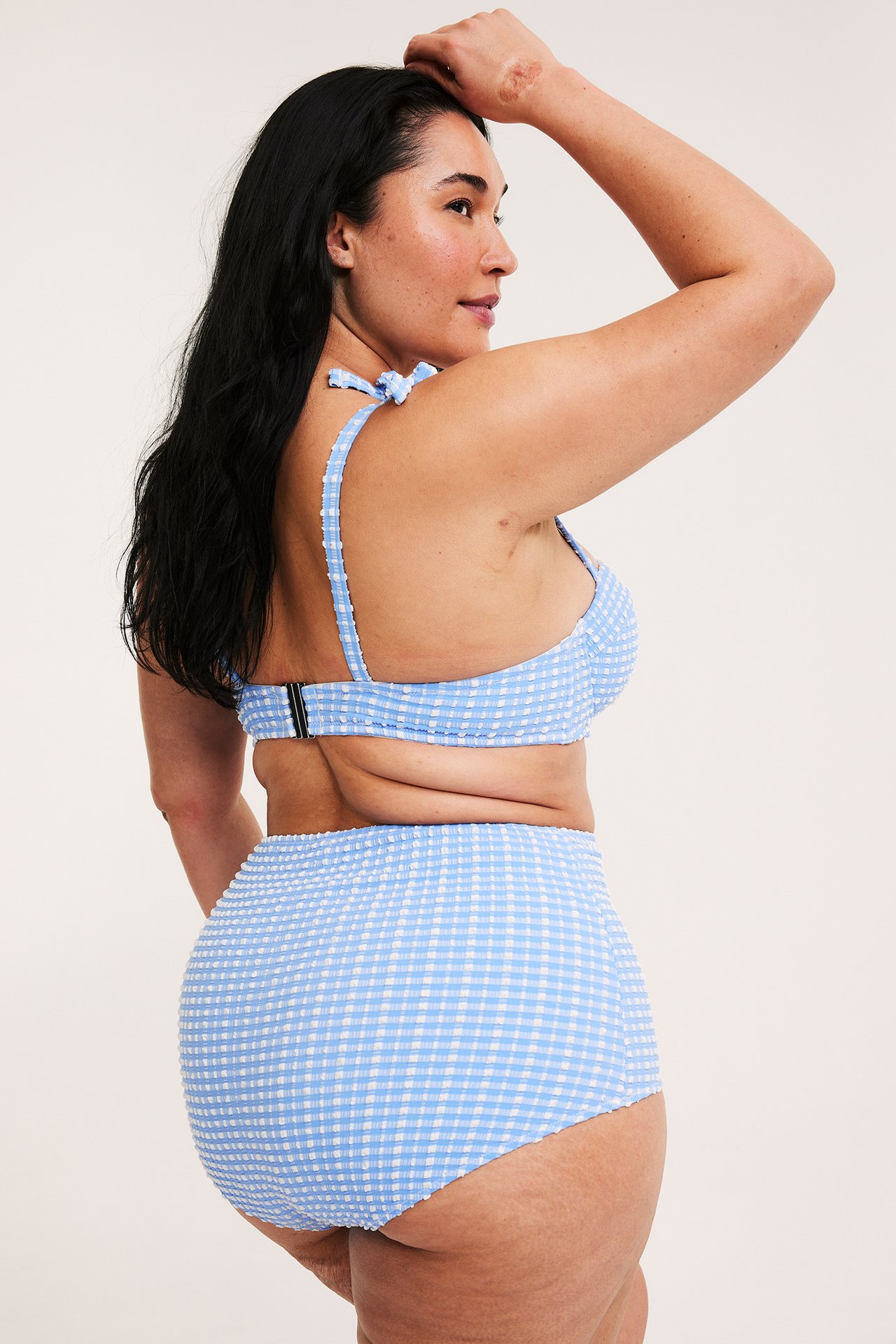 Sidovy av kvinna i ljusblå rutig high-waist bikinitrosa och matchande bikinitopp.