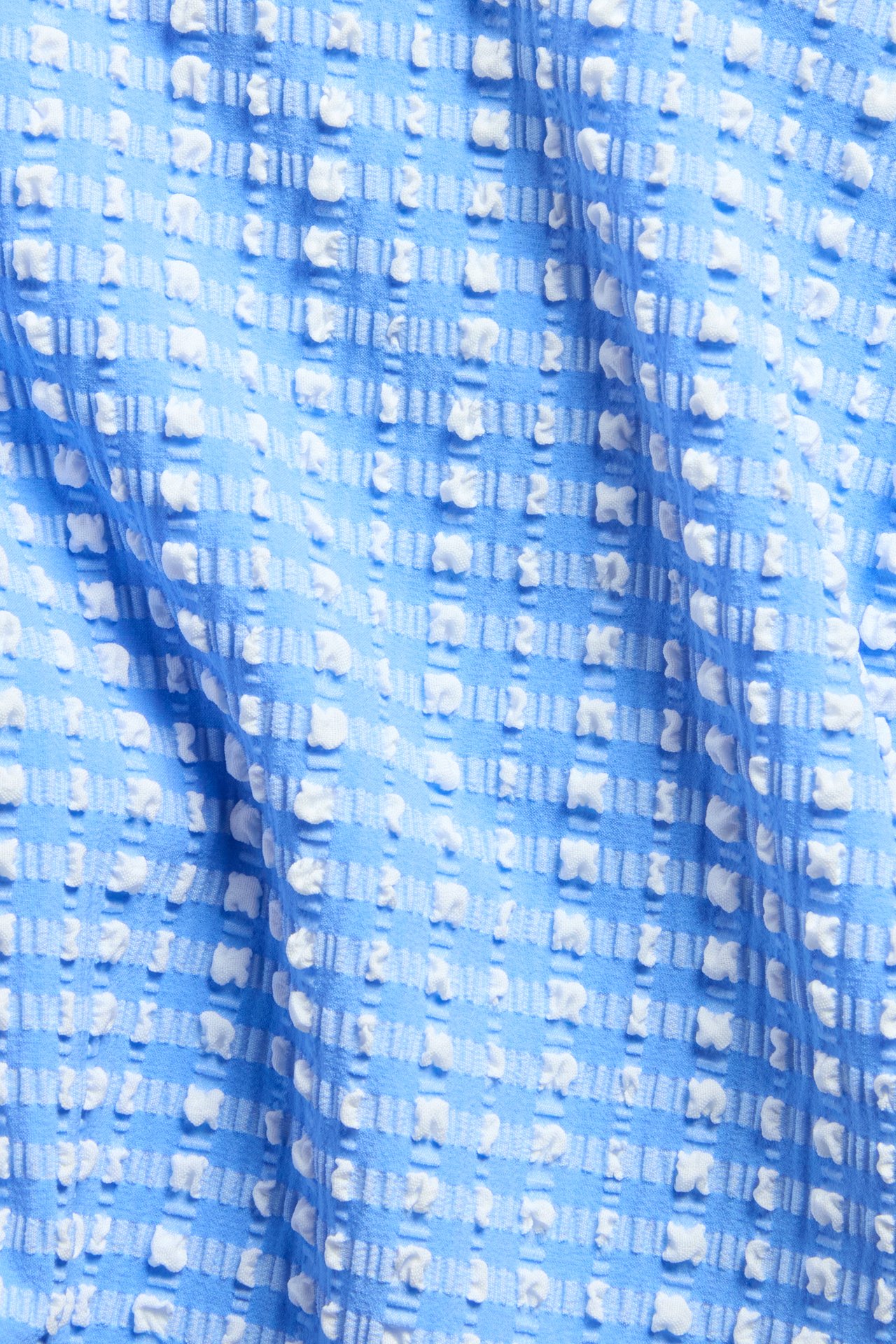 Lähikuva sinivalkoisesta ruudullisesta, kuvioidusta bikinikankaasta kohopisteillä.