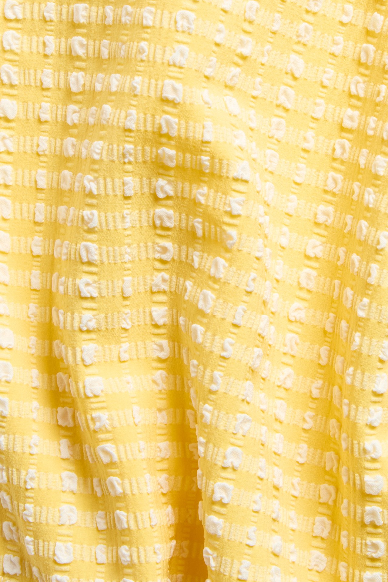 Lähikuva keltaisesta teksturoidusta bikinikankaasta, jossa on kohokuvioitu valkoinen ruudullinen kuvio.