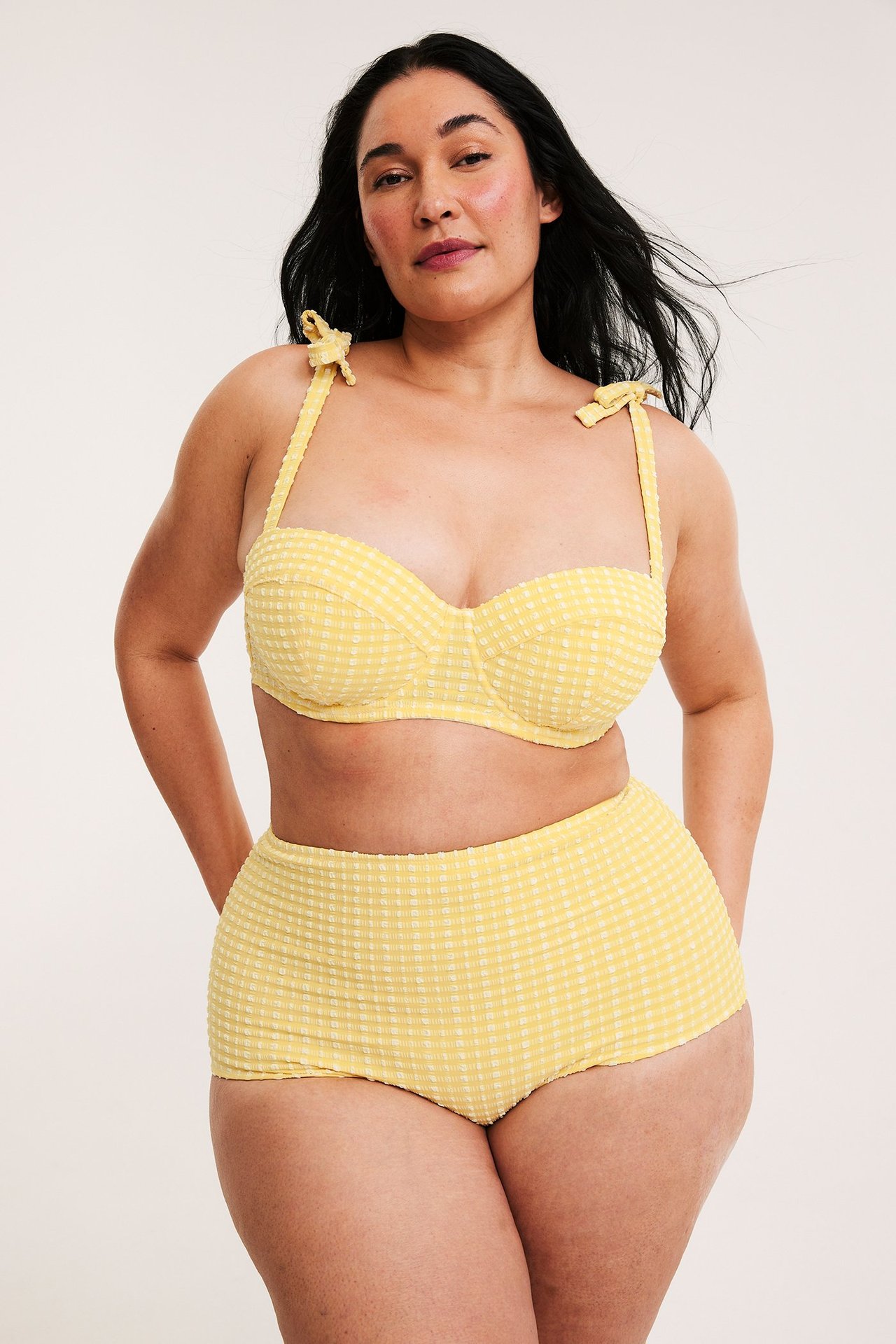 Widok z przodu: kobieta w żółtych, kraciastych figach bikini high-hipster i dopasowanym staniku z wiązanymi ramiączkami.