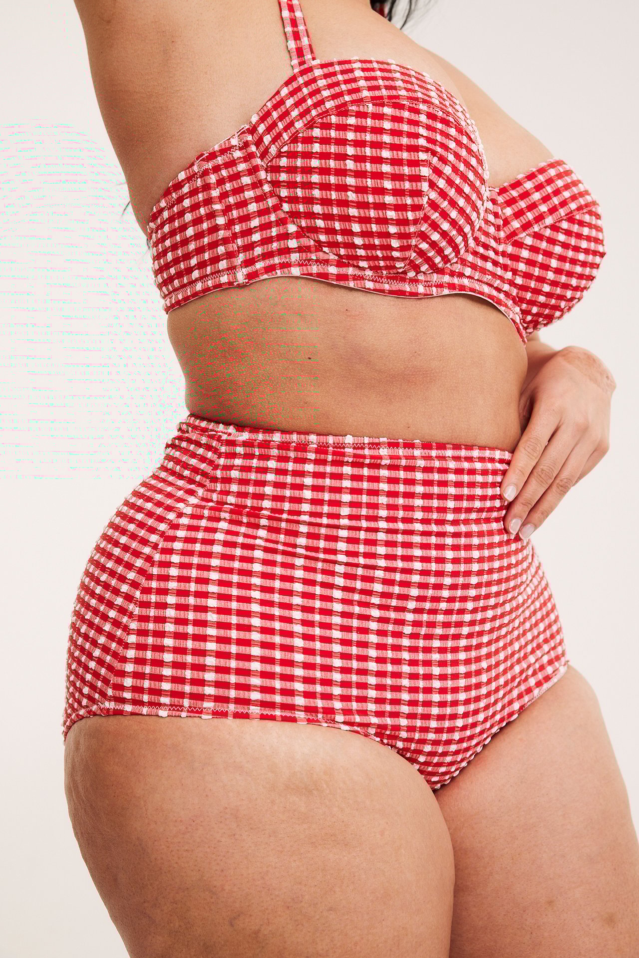 Sidovy av en kvinna som bär röd- och vitrutiga högmidjade bikinitrosor och en matchande bikinitopp.