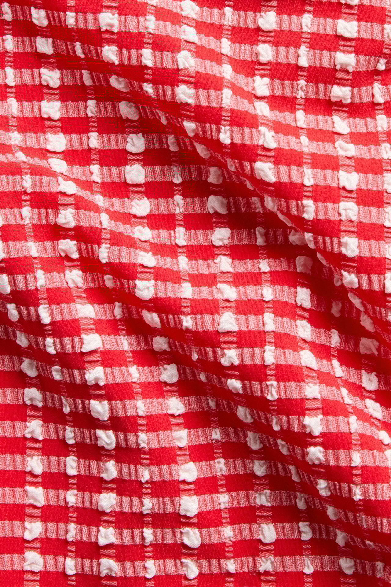 Lähikuva punavalkoisesta ruudullisesta ja tekstuurisesta kankaasta, jossa on nyppyläinen, hieman koholla oleva kuvio.