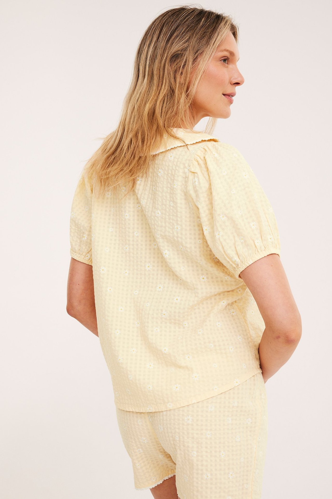 Naisen sivukuva vaaleankeltaisessa kukkakuosisessa vohvelipyjamasarjassa, jossa pitsikaulus.