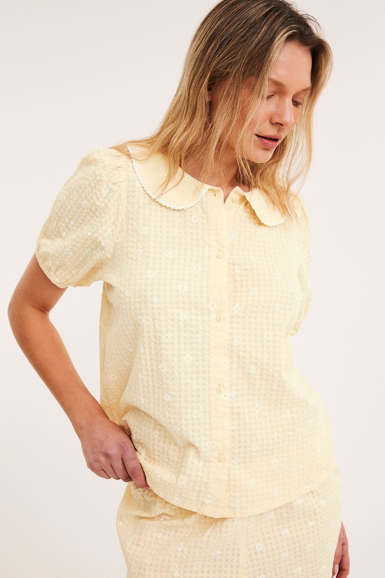 Framsida: Kvinna i ljusgul blommig bäckeböljepyjamaströja med spetskrage och matchande shorts.