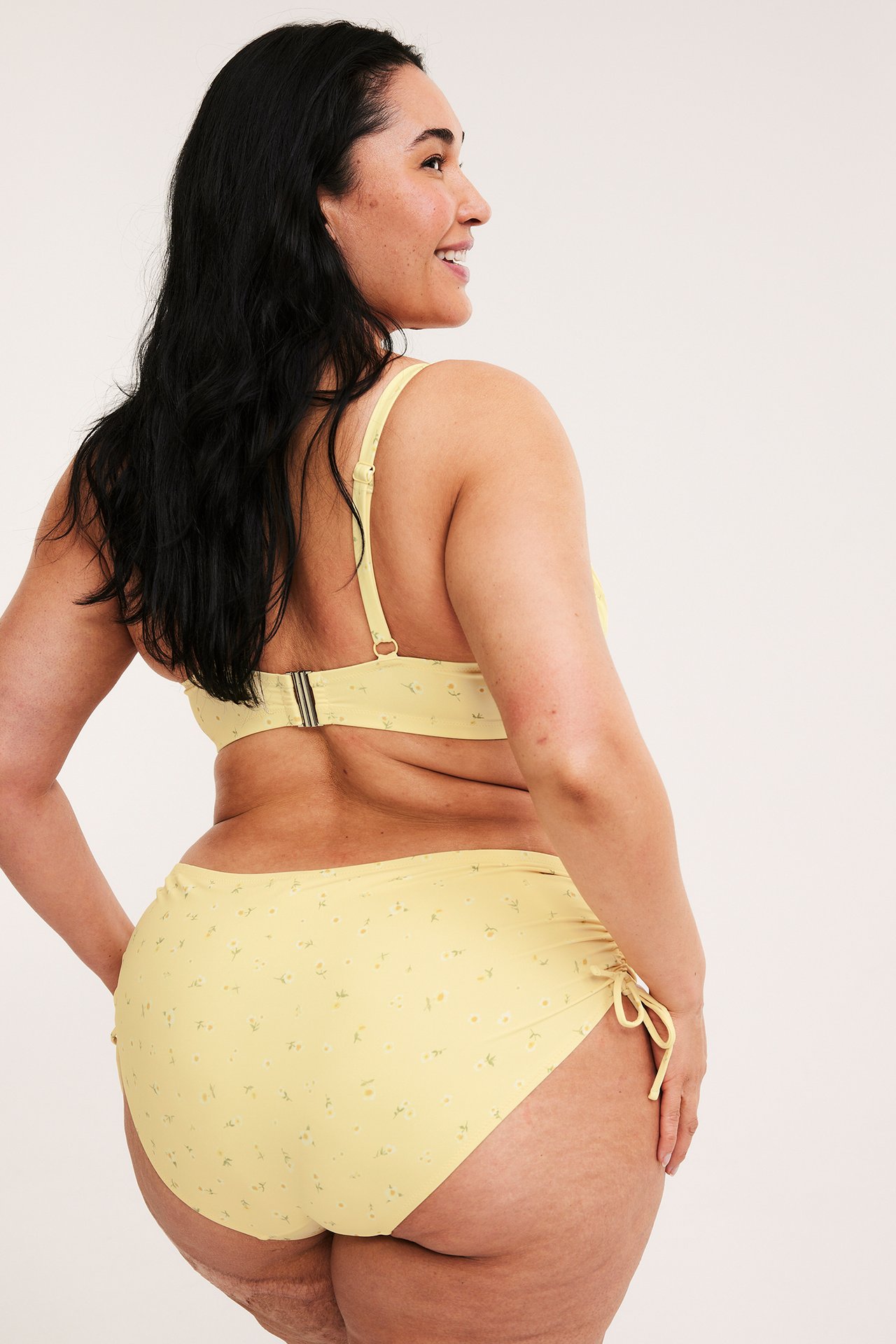 Bakfra, en kvinne i lys beige blomstret hipster bikinitruse med knyting og matchende topp.