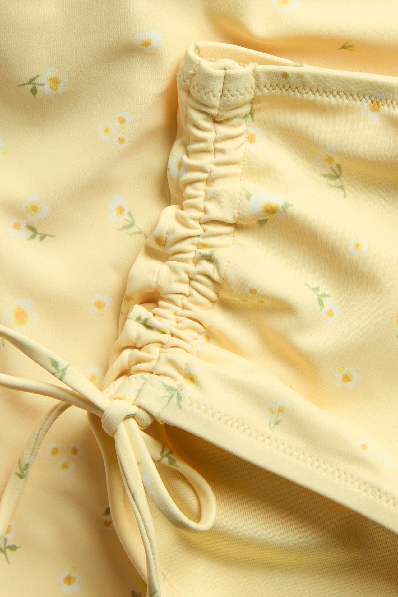 Lähikuva vaaleanbeigestä kukkakuvioisesta hipster-bikinialaosasta, jossa on rypytetty sivu ja säädettävä solmuyksityiskohta.