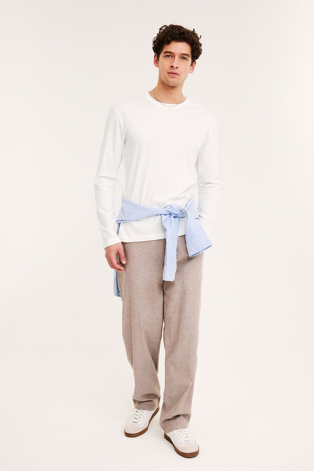 Widok z przodu: Mężczyzna w białym t-shircie z długim rękawem, beżowych spodniach, niebieskiej koszuli w pasie, białych trampkach.