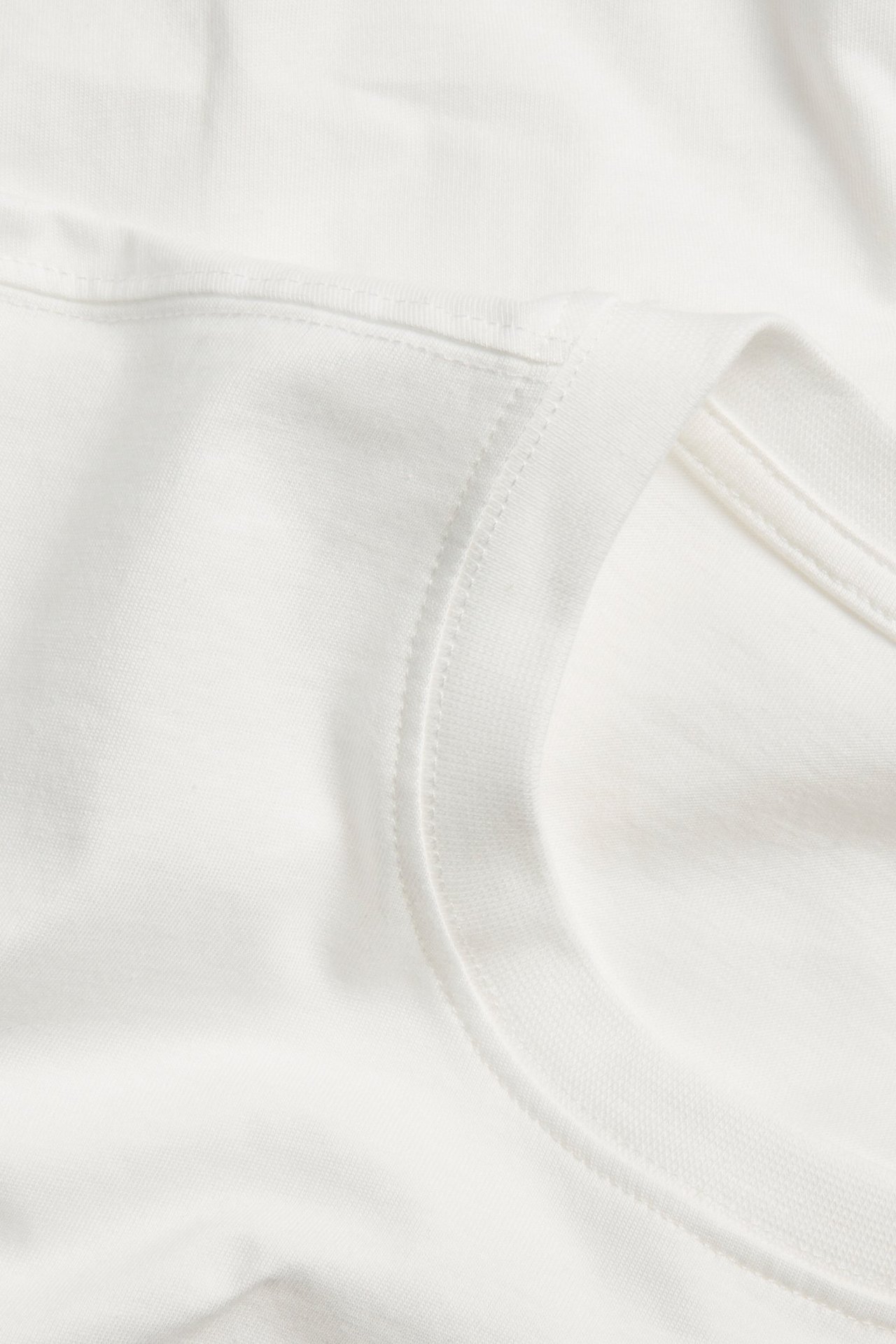 Zbliżenie na off-white, gładki, bawełniany T-shirt z długim rękawem, przedstawiające dekolt i szew na ramieniu.