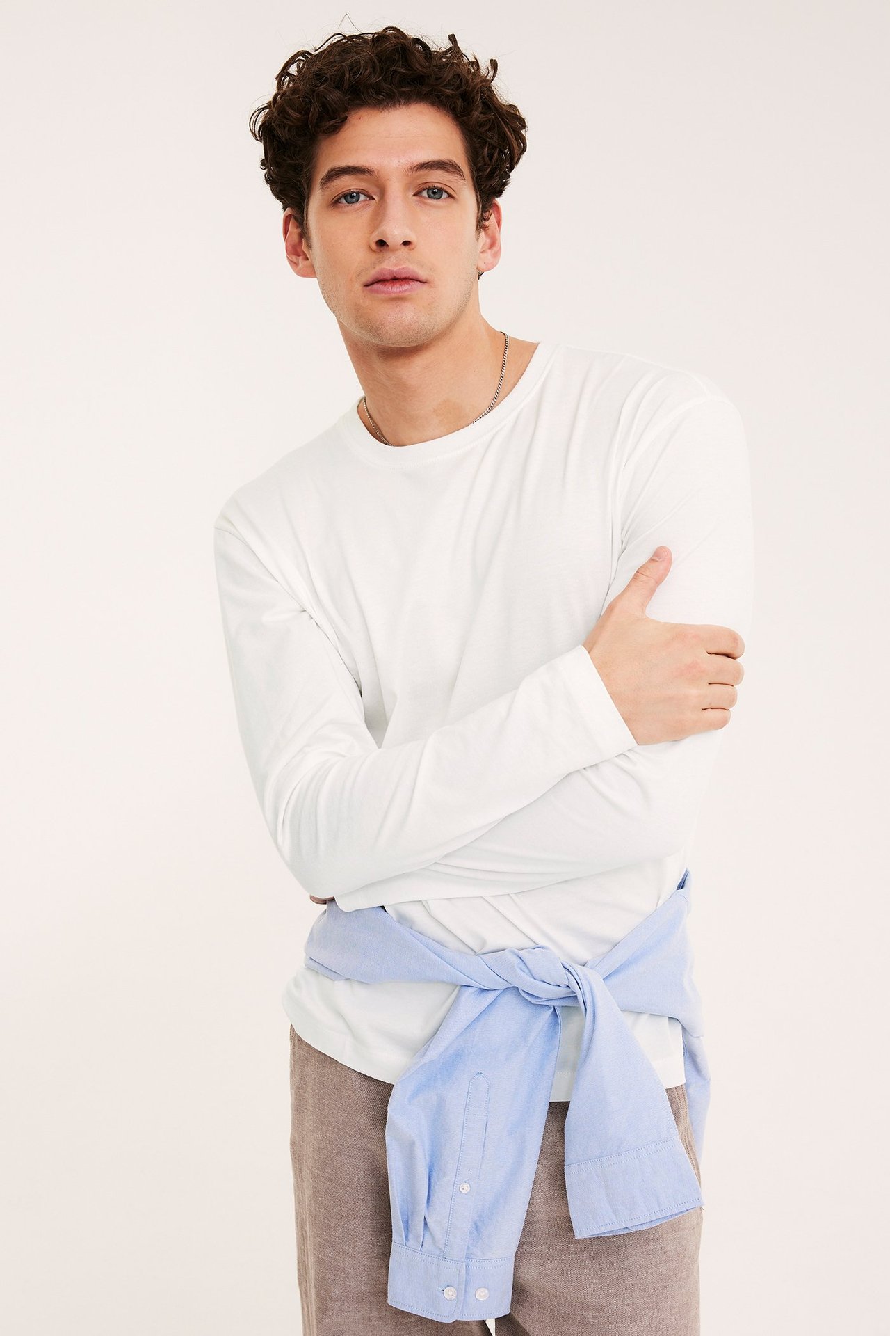Kremowobiała koszulka z długim rękawem na mężczyźnie, z jasnoniebieską koszulą zawiązaną w pasie.