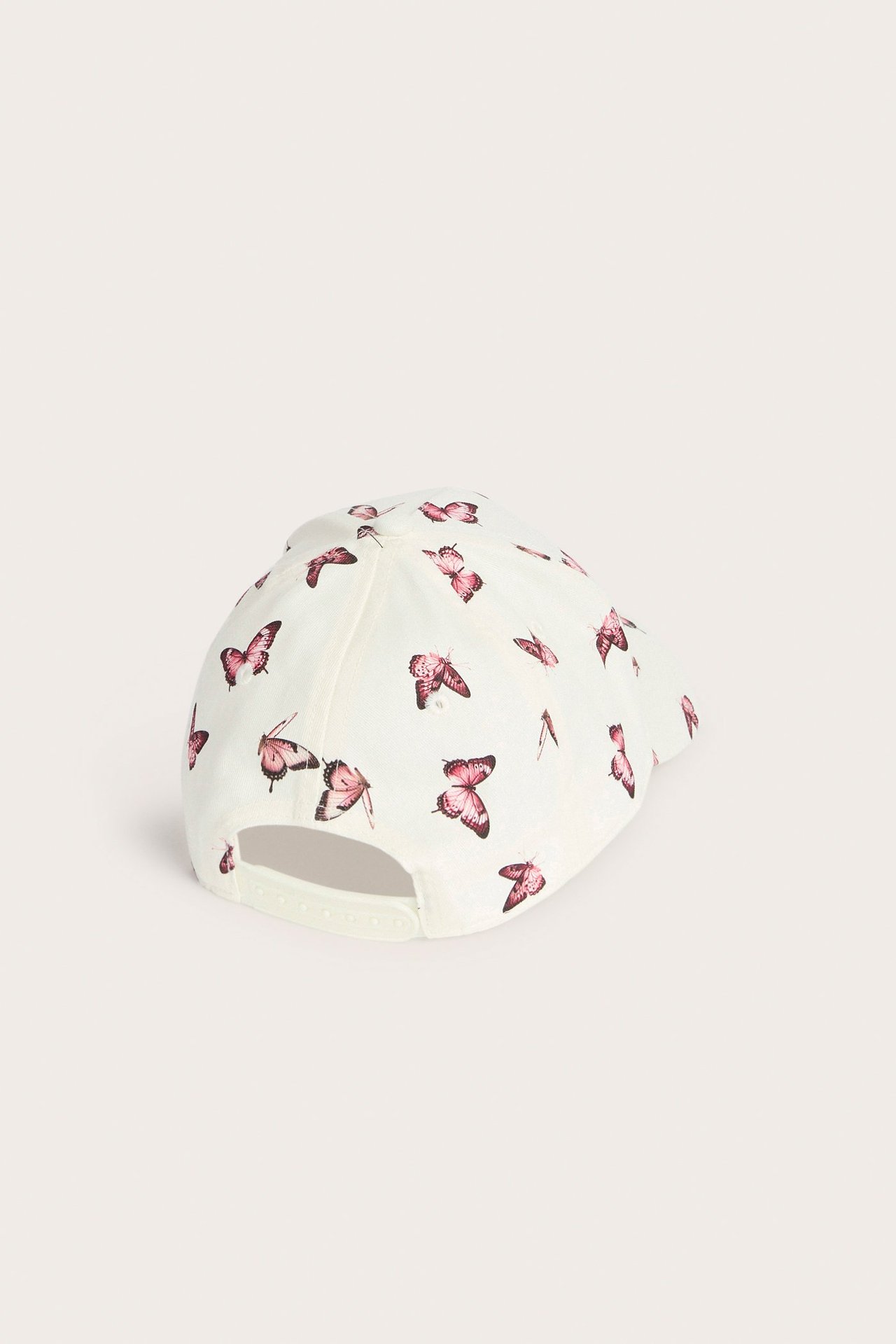 Widok z tyłu: Kremowa czapka dziecięca z różowym wzorem motyli i regulowanym zapięciem.