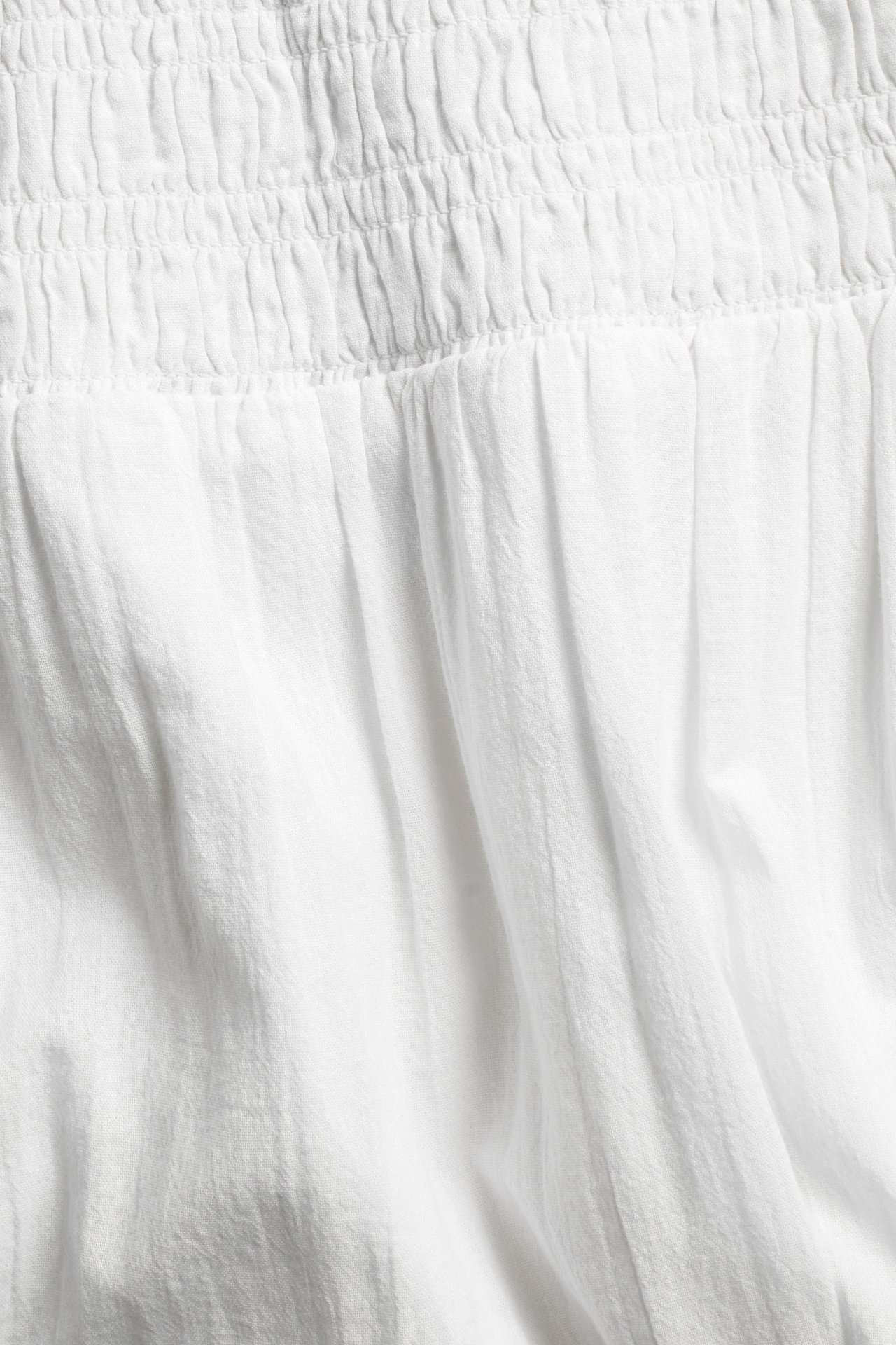 Lähikuva valkoisesta strukturoidusta puuvillamaksi-hameesta, jossa smock-vyötärö ja rypytyksiä.