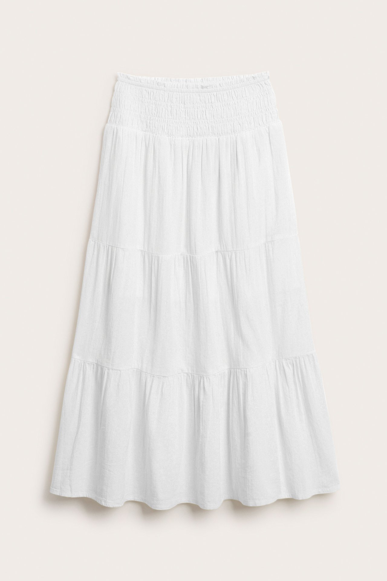 Edestä näkymä valkoisesta, pehmeästä puuvillaisesta maksihameesta, jossa on smokkivyötärö ja röyhelöitä.